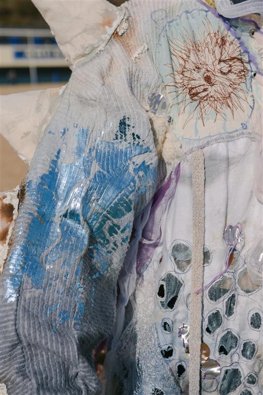 A person wearing a pollution-inspired dress on Bournemouth beach, blue, green and white with patterns and embroidery, close-up