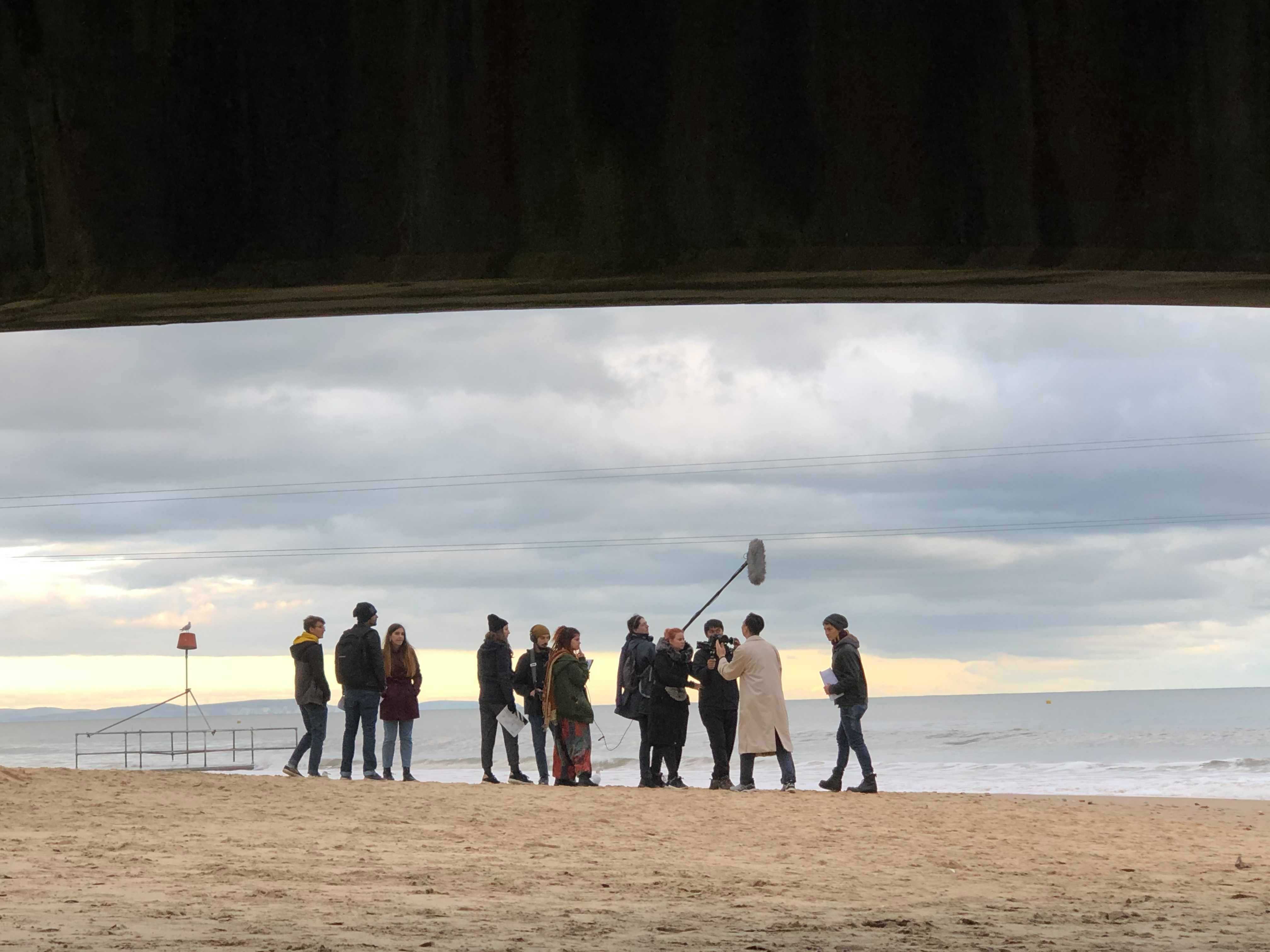 A film crew gathering on a beach in the distance.