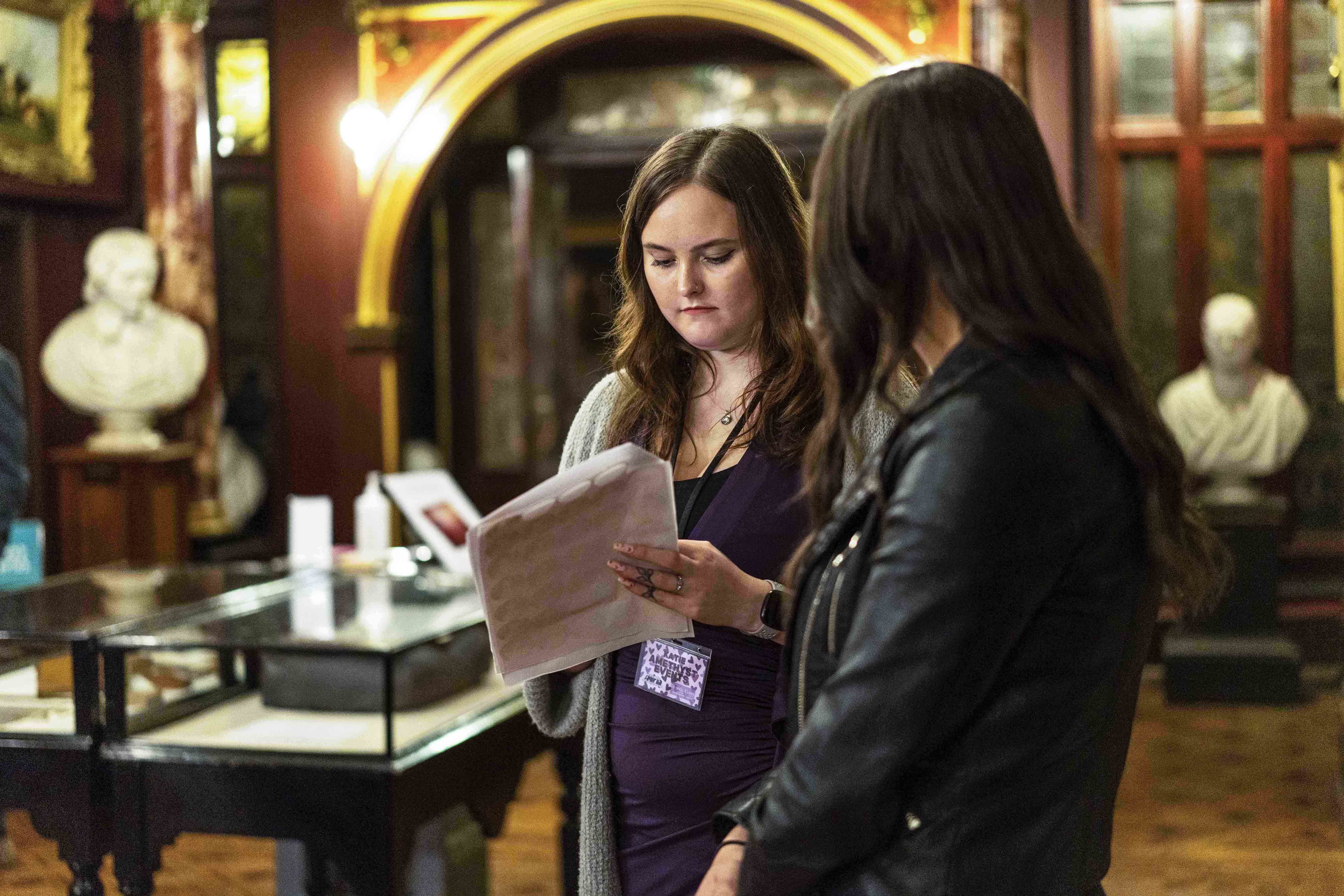 Two people looking at a document while standing in a mansion museum space.