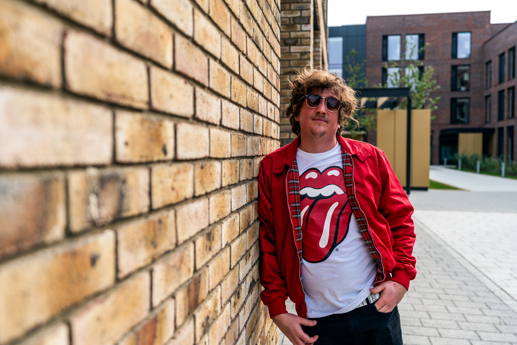 Headshot of DD Allen posing next to a brick wall and standing in a university courtyard.