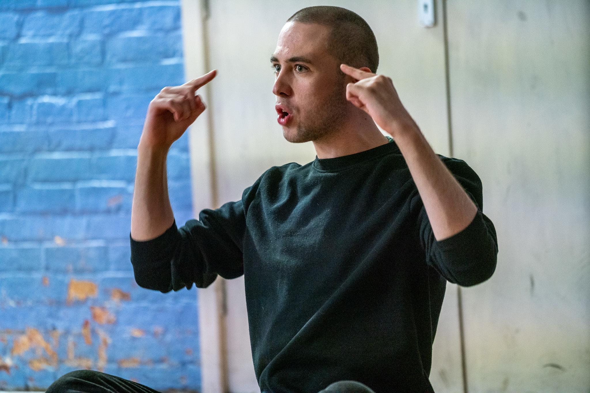 An actor in the middle of a line points towards their head with both hands.