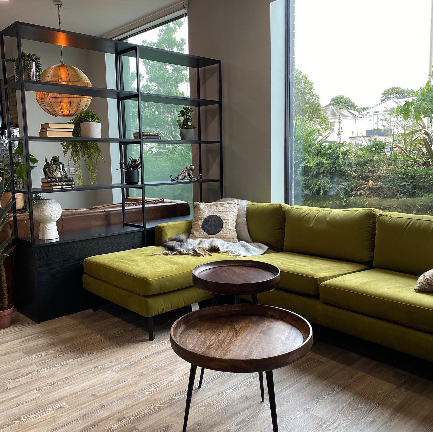 A green sofa and decorations in front of a large window.
