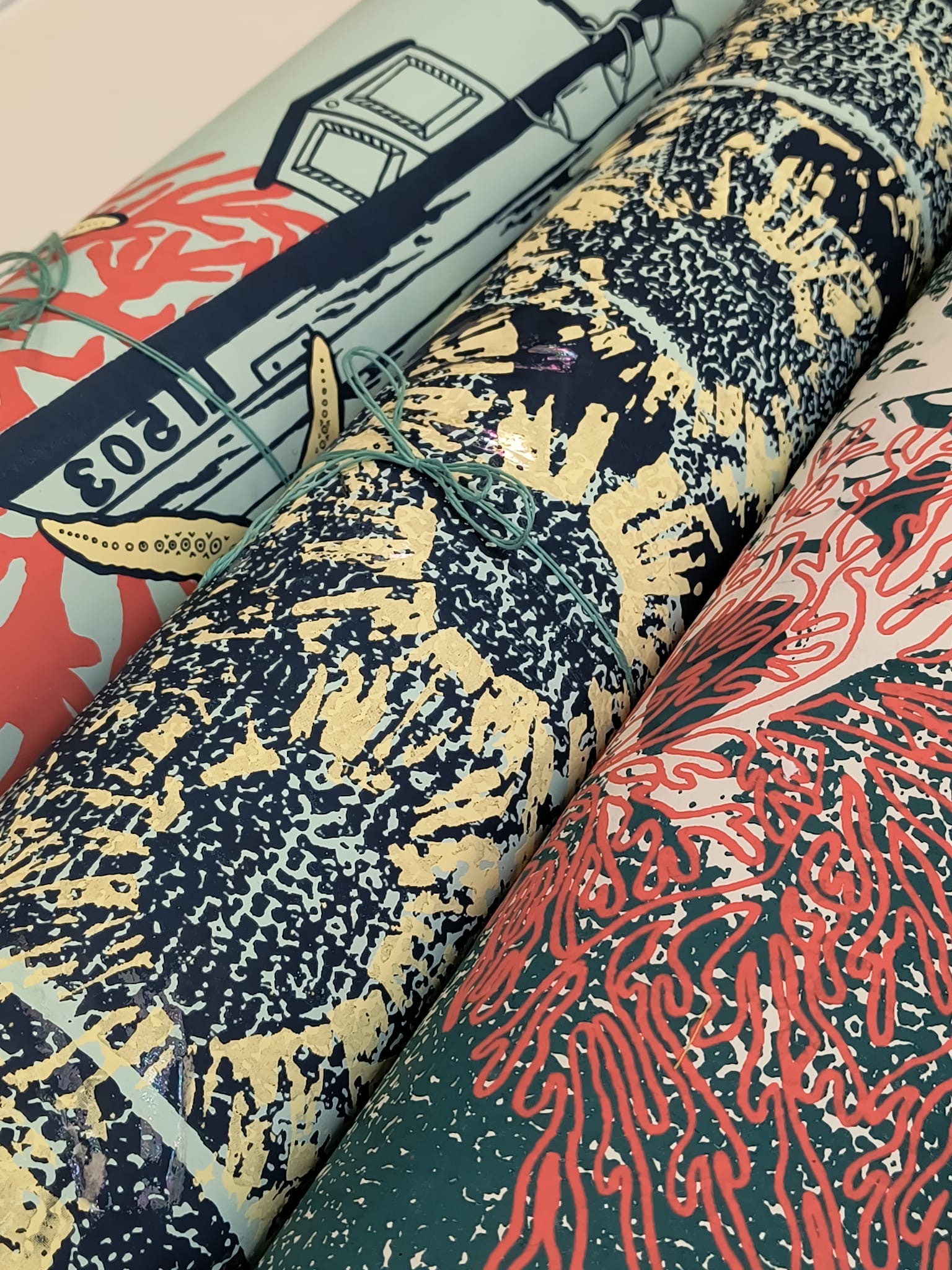 Rolled prints with textured patterns in yellow, black, coral pink, and green. Grey illustrated gun with "SOCIAL" text visible on left.