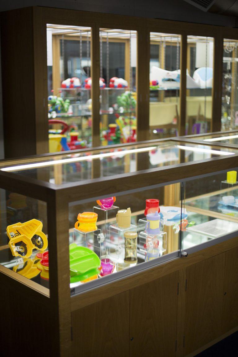 Several plastic objects on display inside a glass museum exhibition cabinet, viewed from a diagonal.