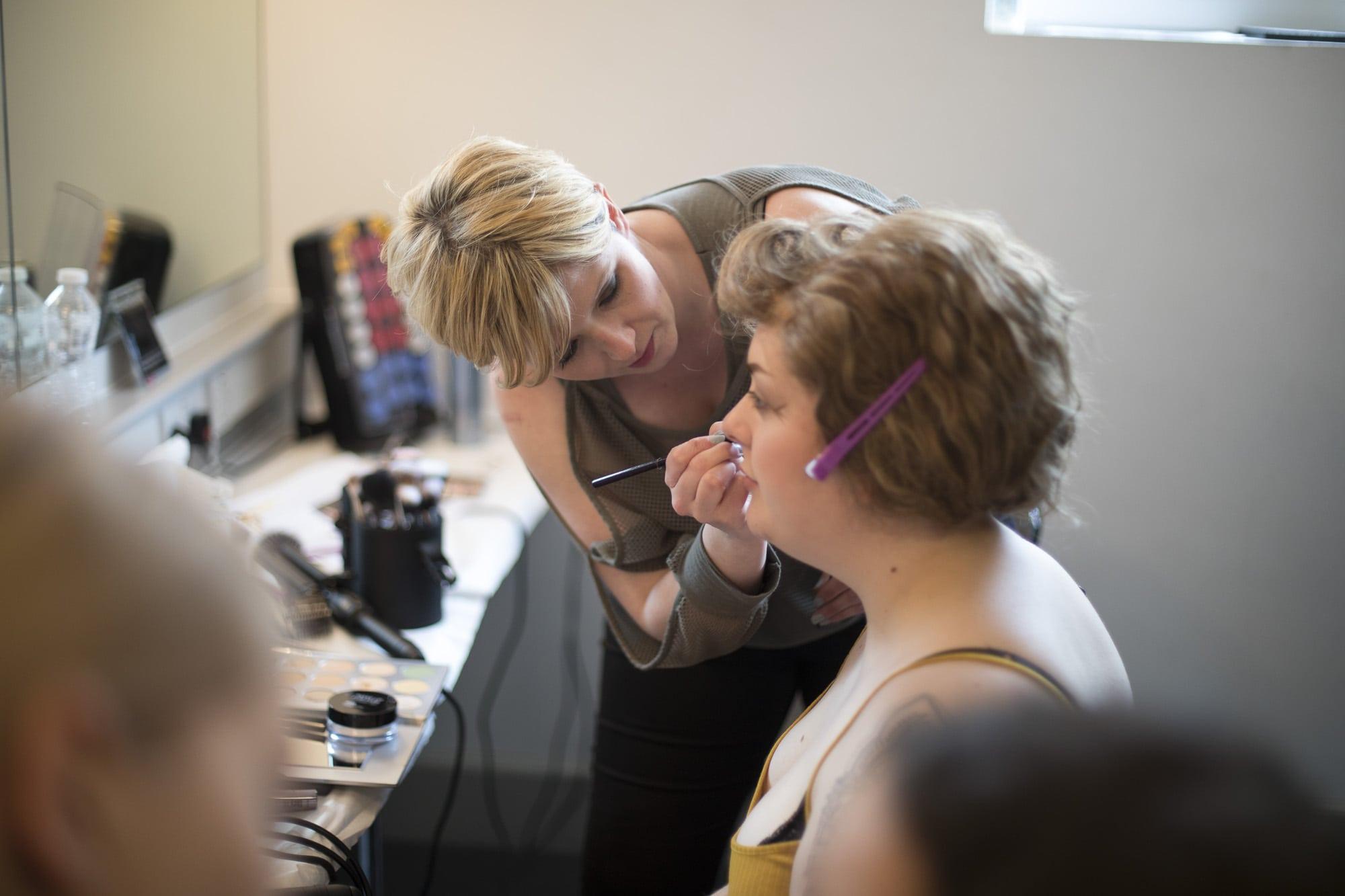 A person sits in a makeup studio while a makeup artist works on their face.