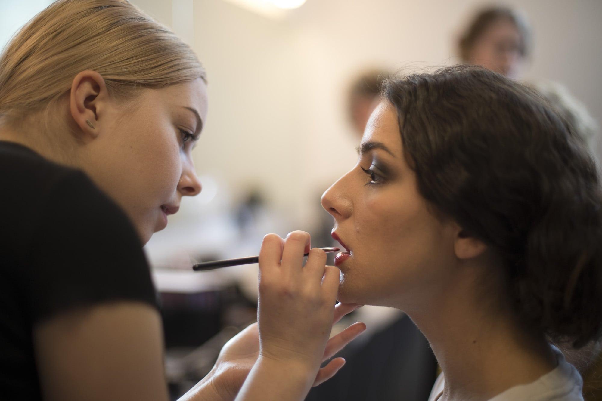 A makeup artist works on a model's lips.