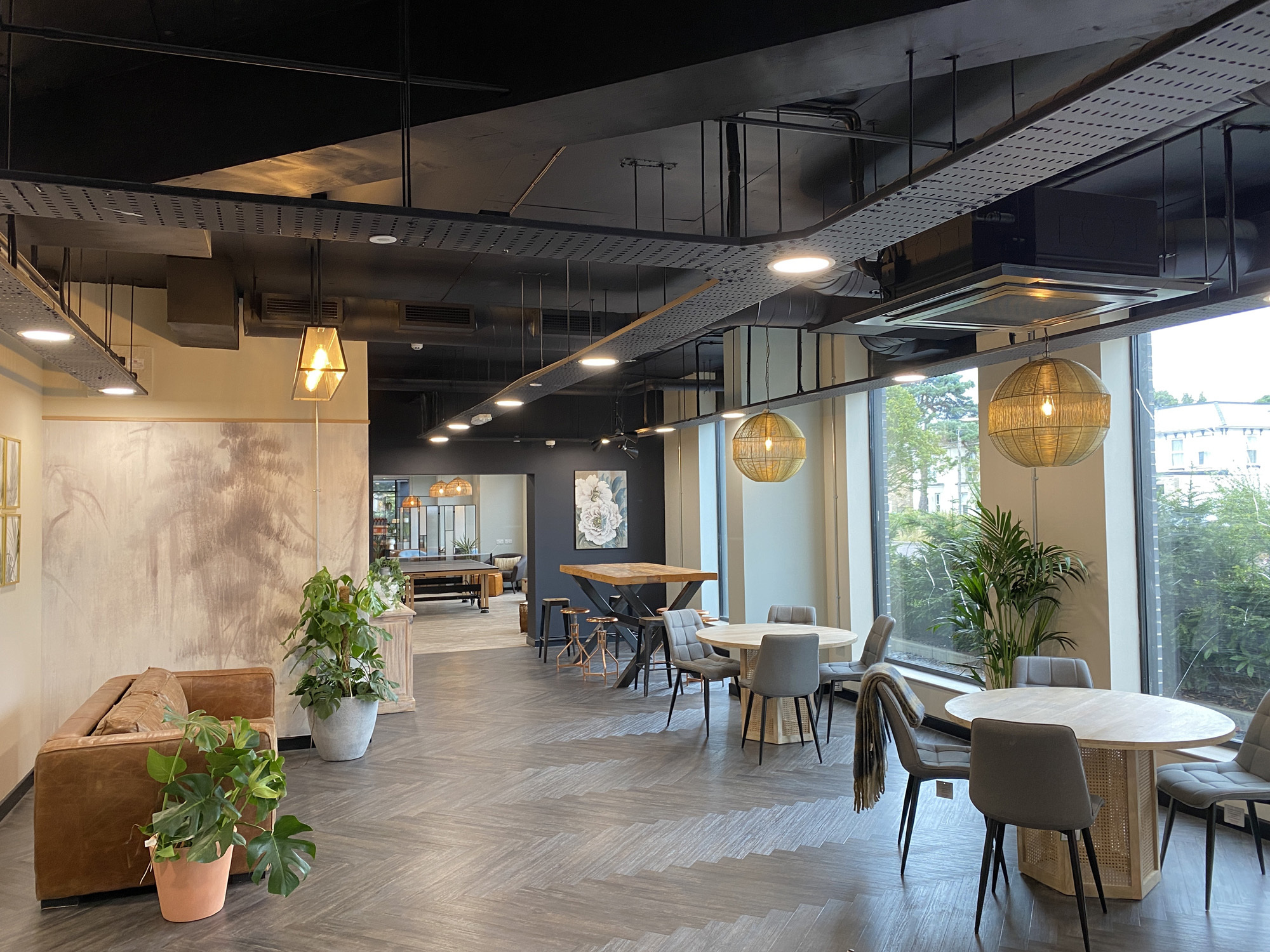 Student accommodation lobby with plants, tables, ambient lighting and large windows.