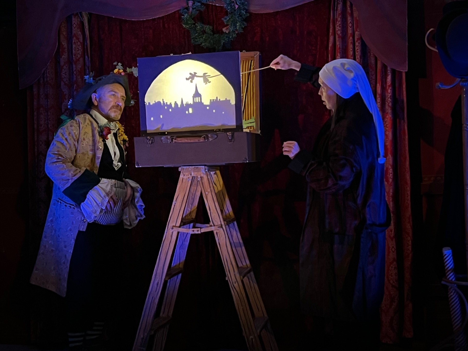 Two actors performing in 'A Christmas Carol', standing either side of a moonlit scene balanced on a ladder