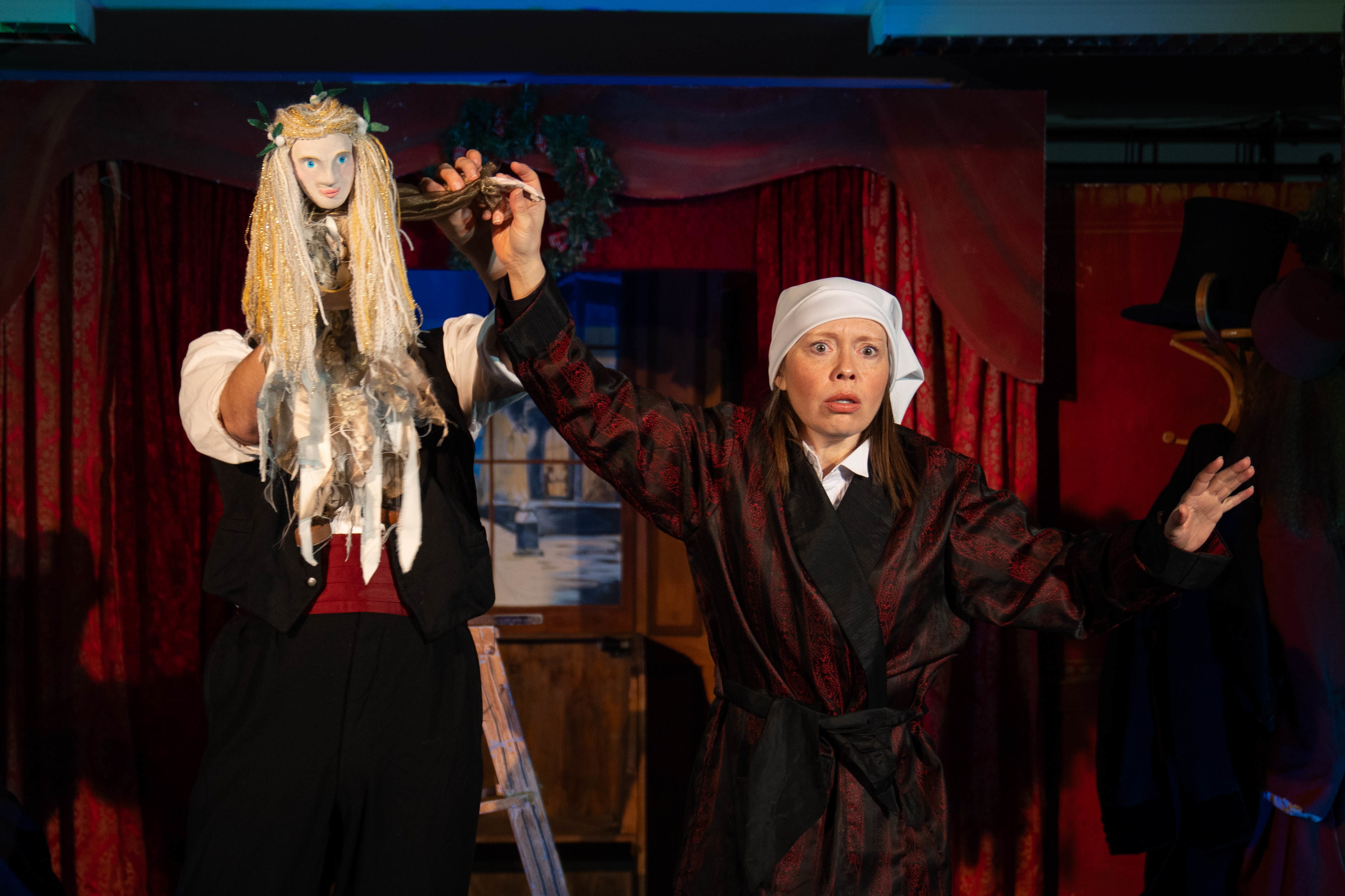 Actress L Garland in costume as Ebenezer Scrooge, holding the hand of a puppet of the Ghost of Christmas Past.