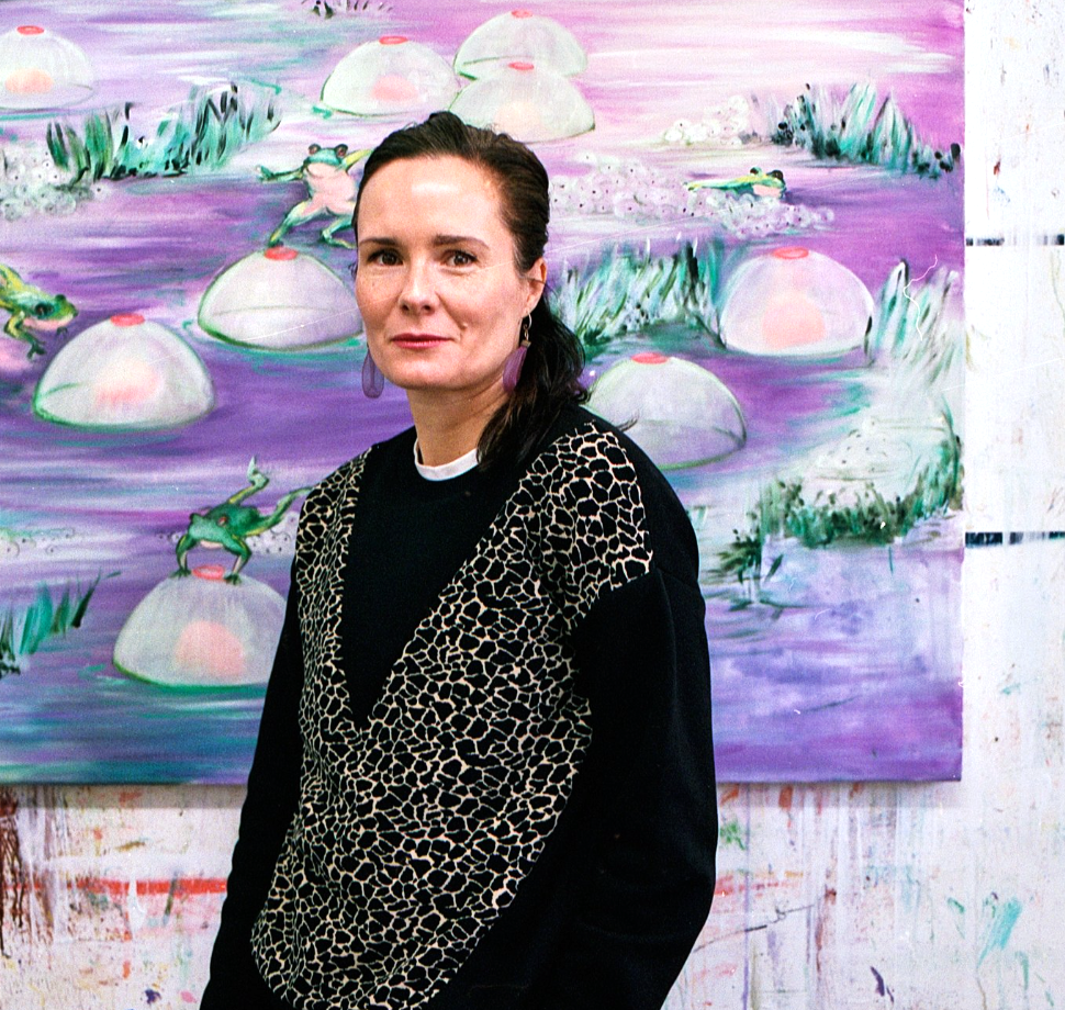 Woman in black patterned jacket standing before large painting with purple background, white circular forms, and green brushstrokes.