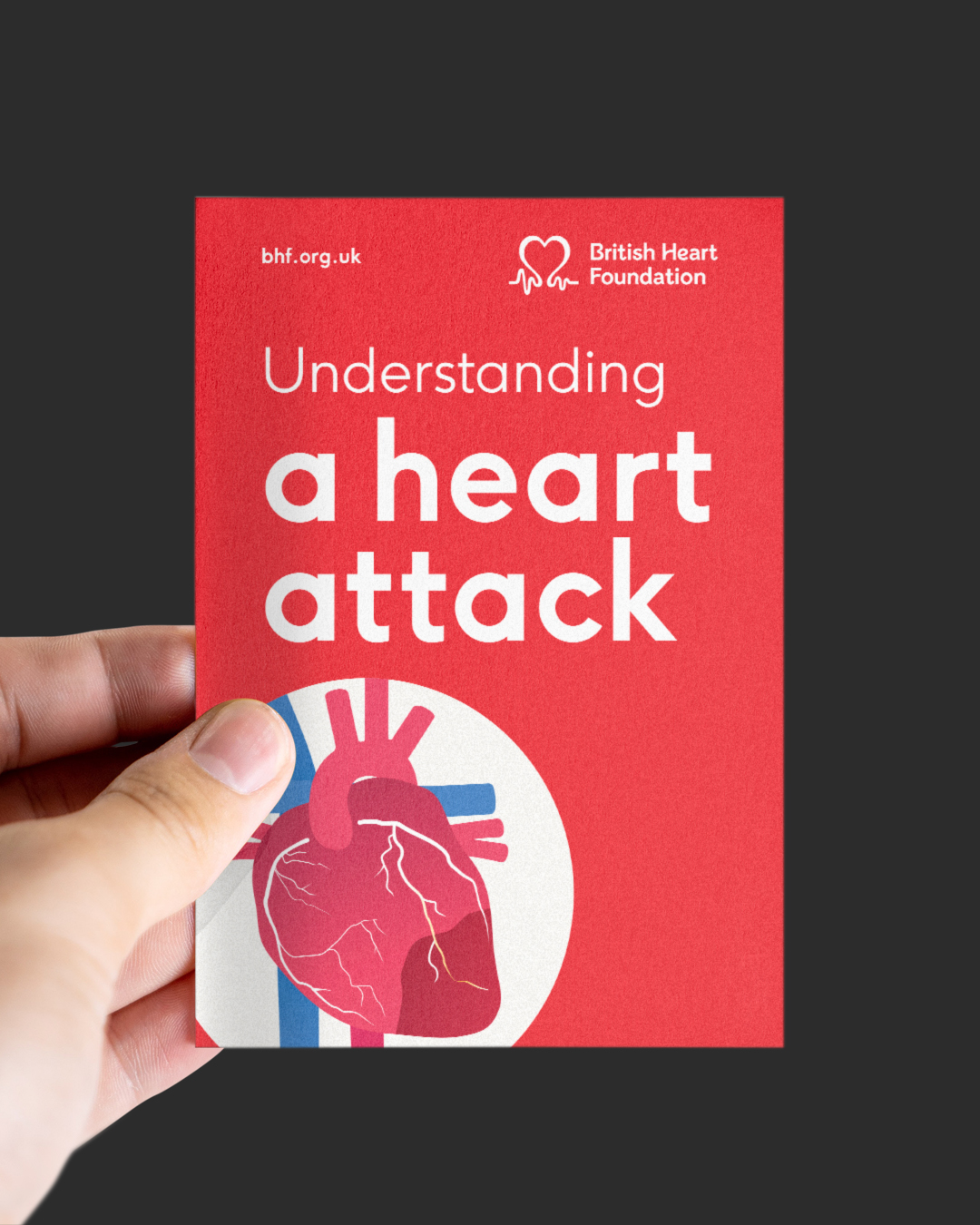 A hand holds a red British Heart Foundation leaflet titled 'Understanding a heart attack', with a heart illustration on a dark background.