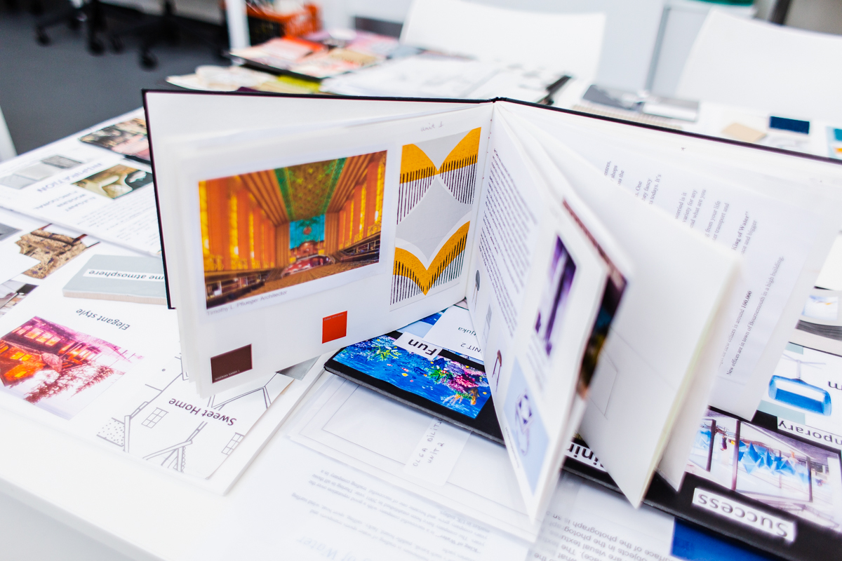 A portfolio book open showing two pages of work. The book is propped up on top of documents and other pieces of work.