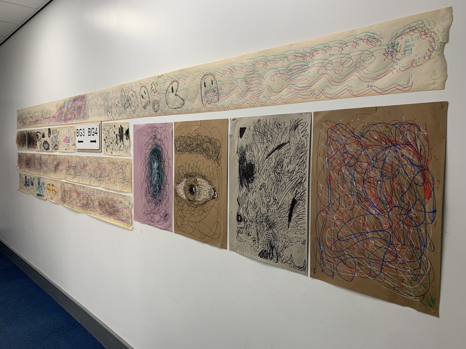 A series of pieces of artwork is arranged on a gallery wall, viewed from the side