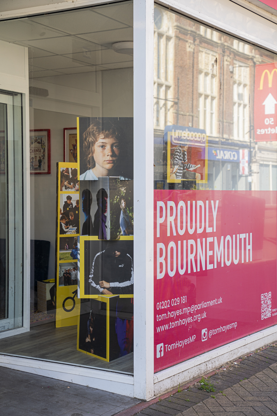 A brightly coloured shop window displaying a promotional banner for Bournemouth, featuring a large photo of a boy and various smaller images arranged on a stand. The background shows a street with a McDonald's restaurant visible.