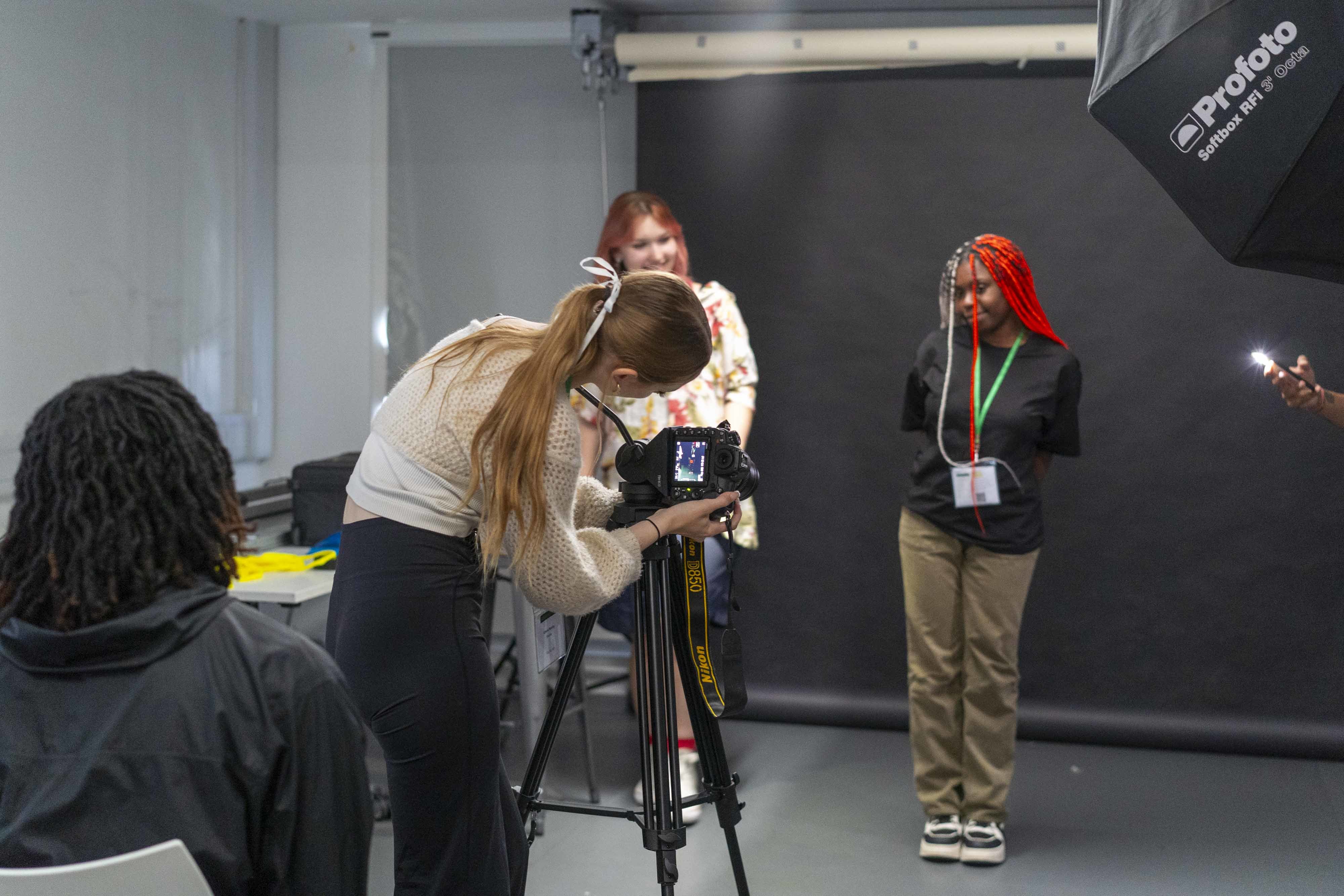 4 students in a photography studio, one is modelling and another is operating a camera