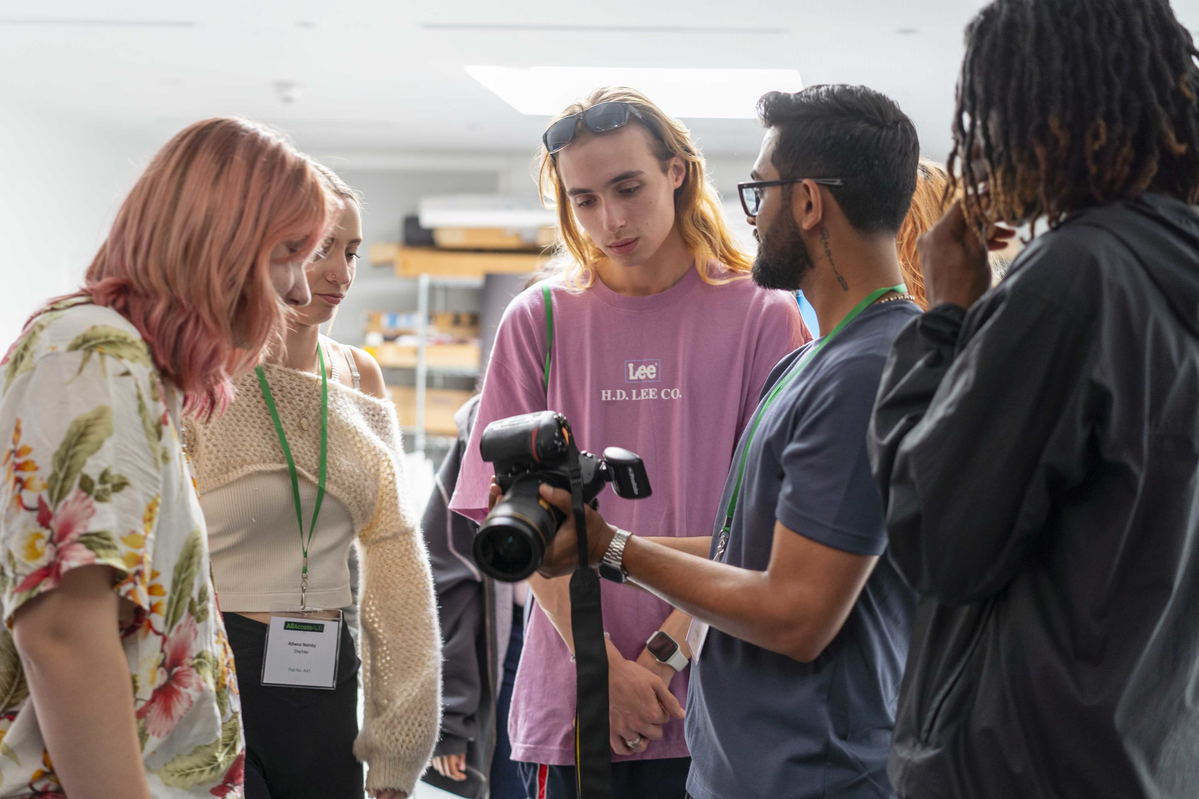 4 students watching a demonstration from their photography tutor holding a digital camera