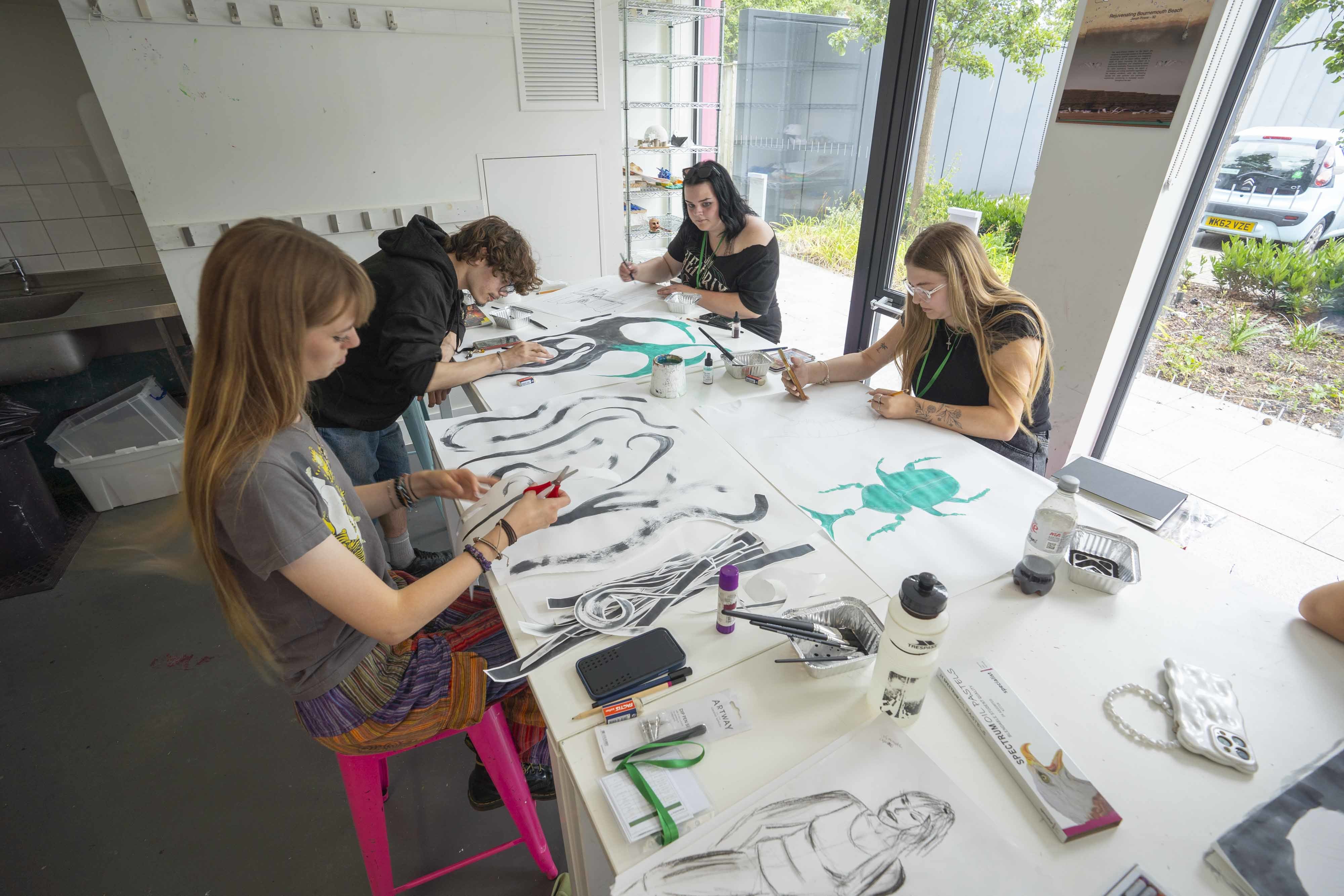 4 students in a studio working on large pieces of paper with black and blue paint