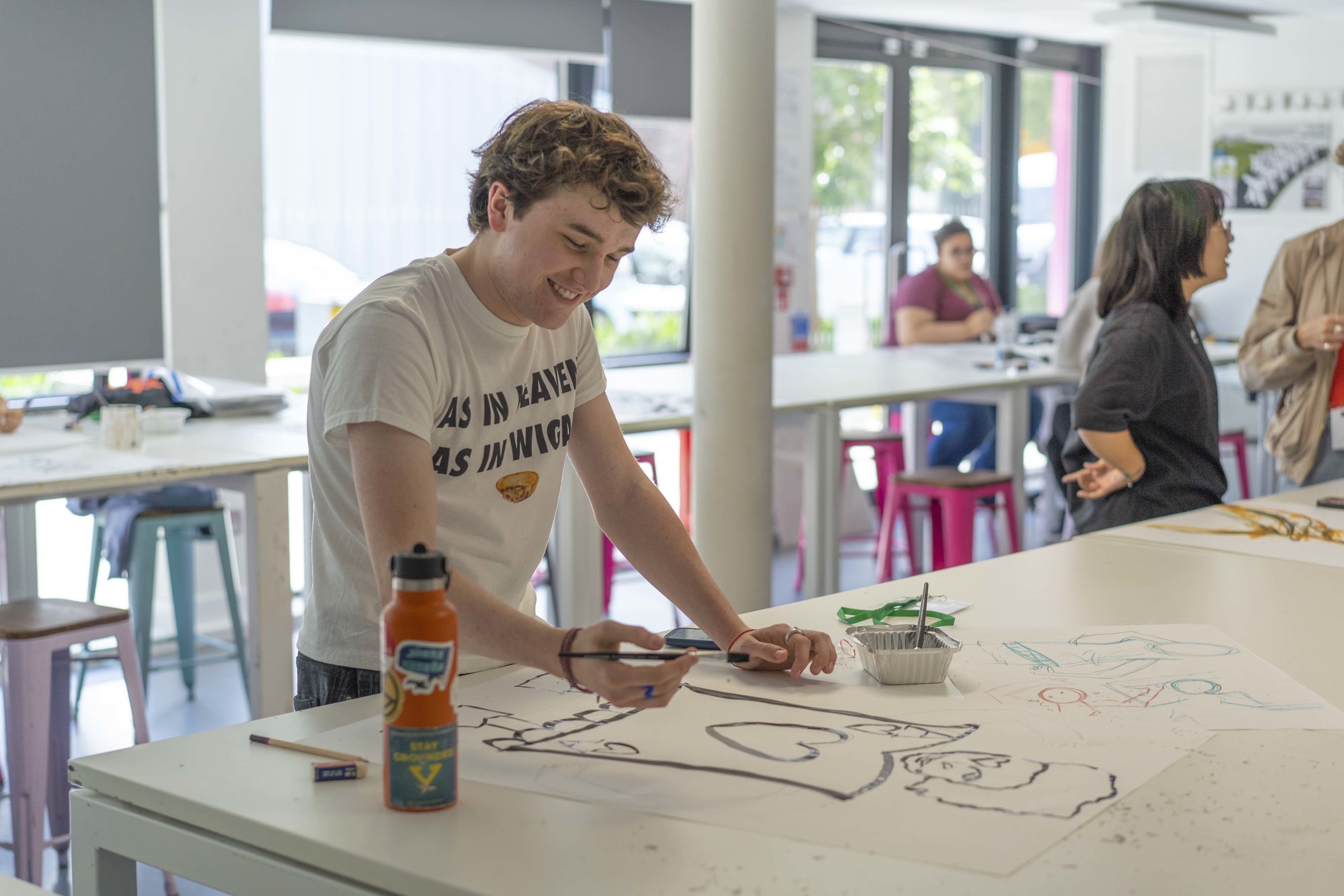 A student in a white t shirt painting a portrait in black ink on a large white pieces of paper