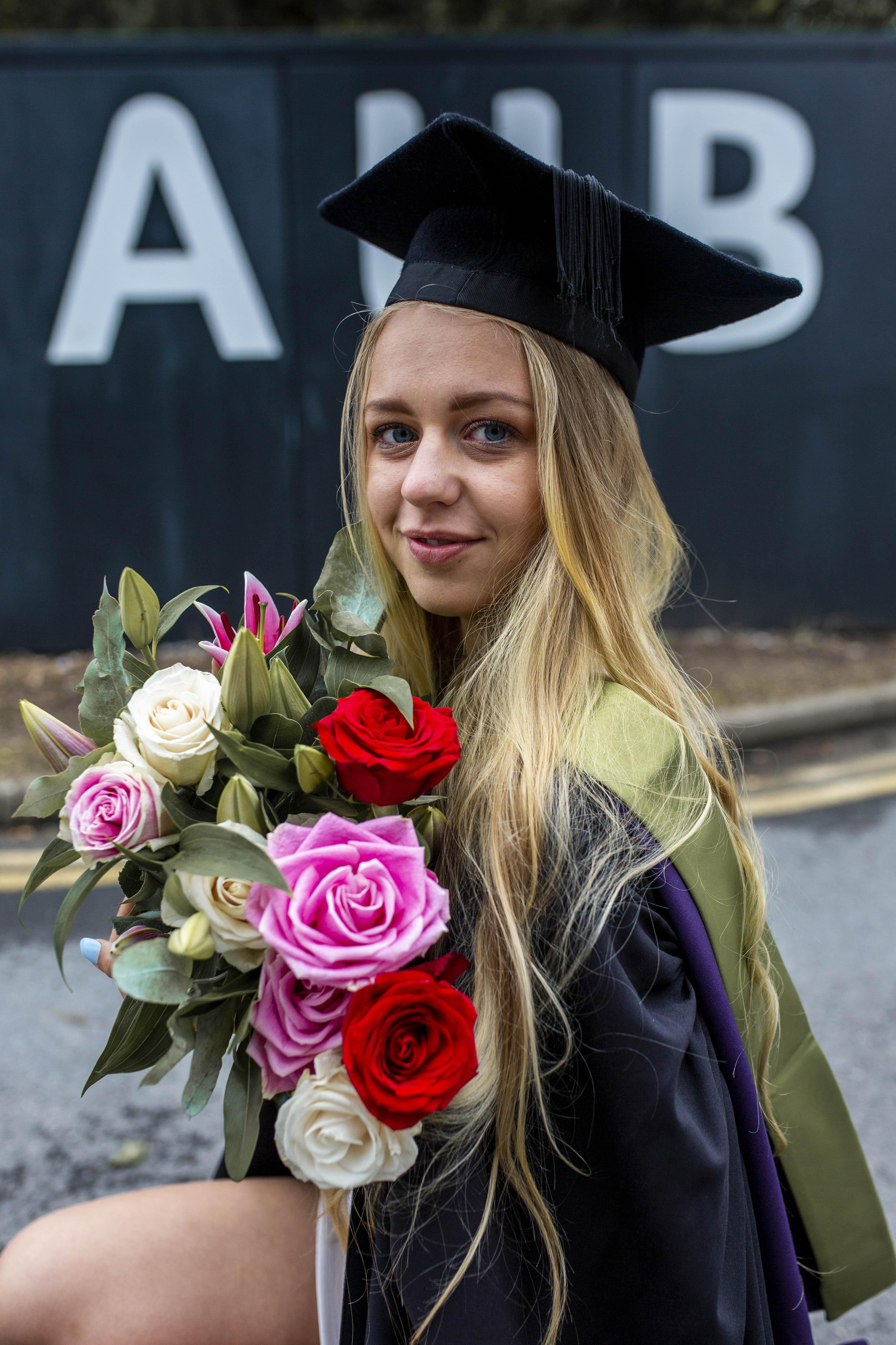 Headshot of AUB Photography graduate Deimante Aleks. She is sitting side-face in graduation clothes and holding a bouquet of flowers.