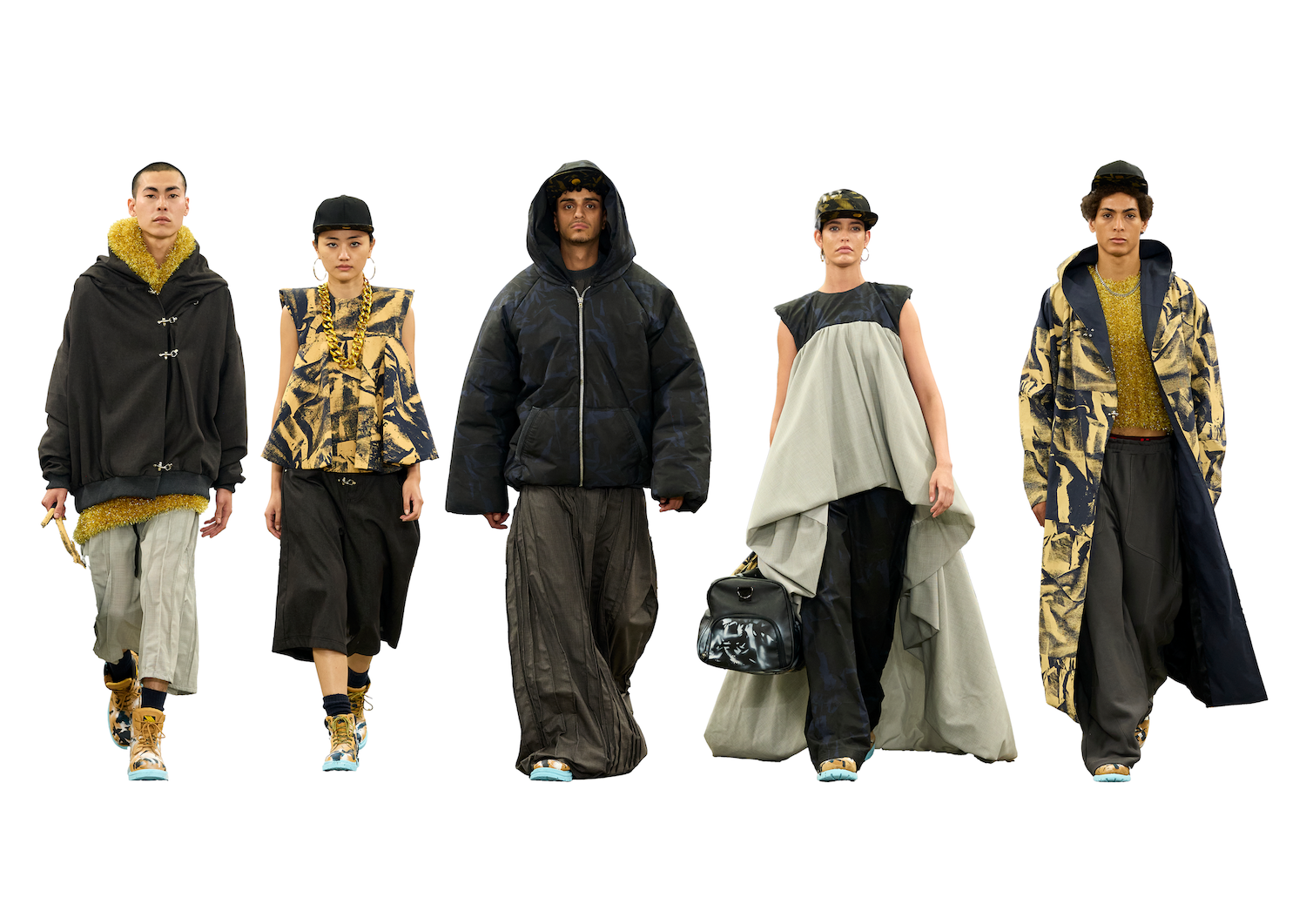 Five models walking in a fashion show, showcasing diverse outfits. The first model wears a black hoodie, the second a patterned top, the third a puffer jacket, the fourth a flowing grey dress, and the fifth a long patterned coat. The background is white.