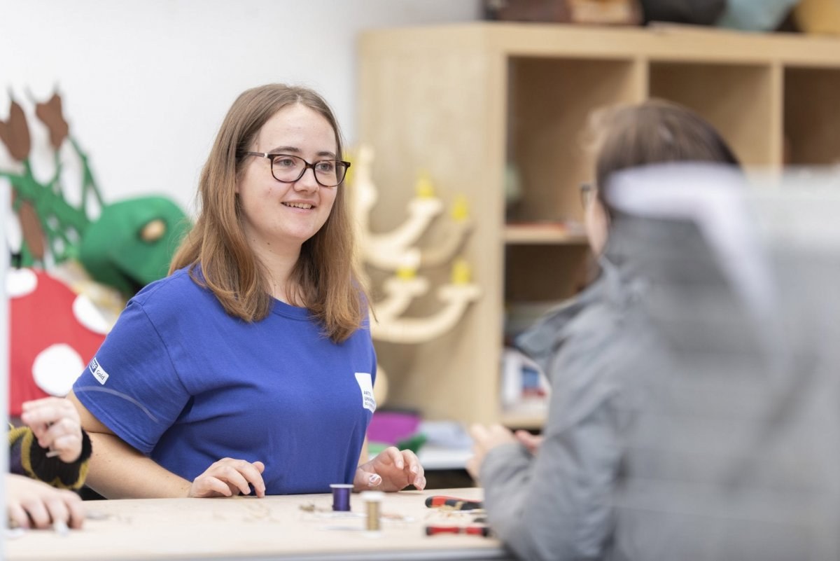 Student ambassador sits at a table and helps out at an open day workshop.