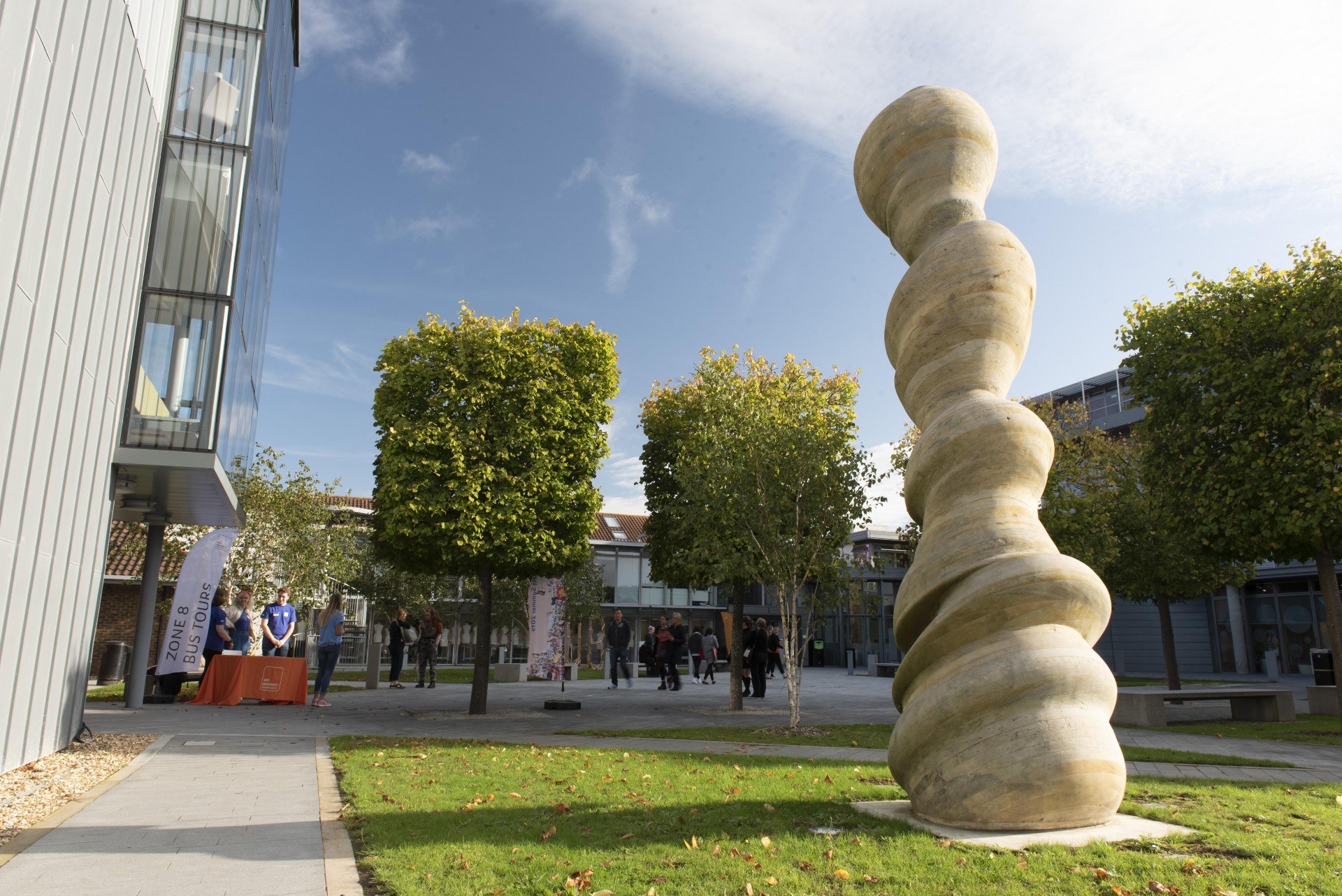 Abstract sculpture on a university campus, with trees cut into squares behind it.