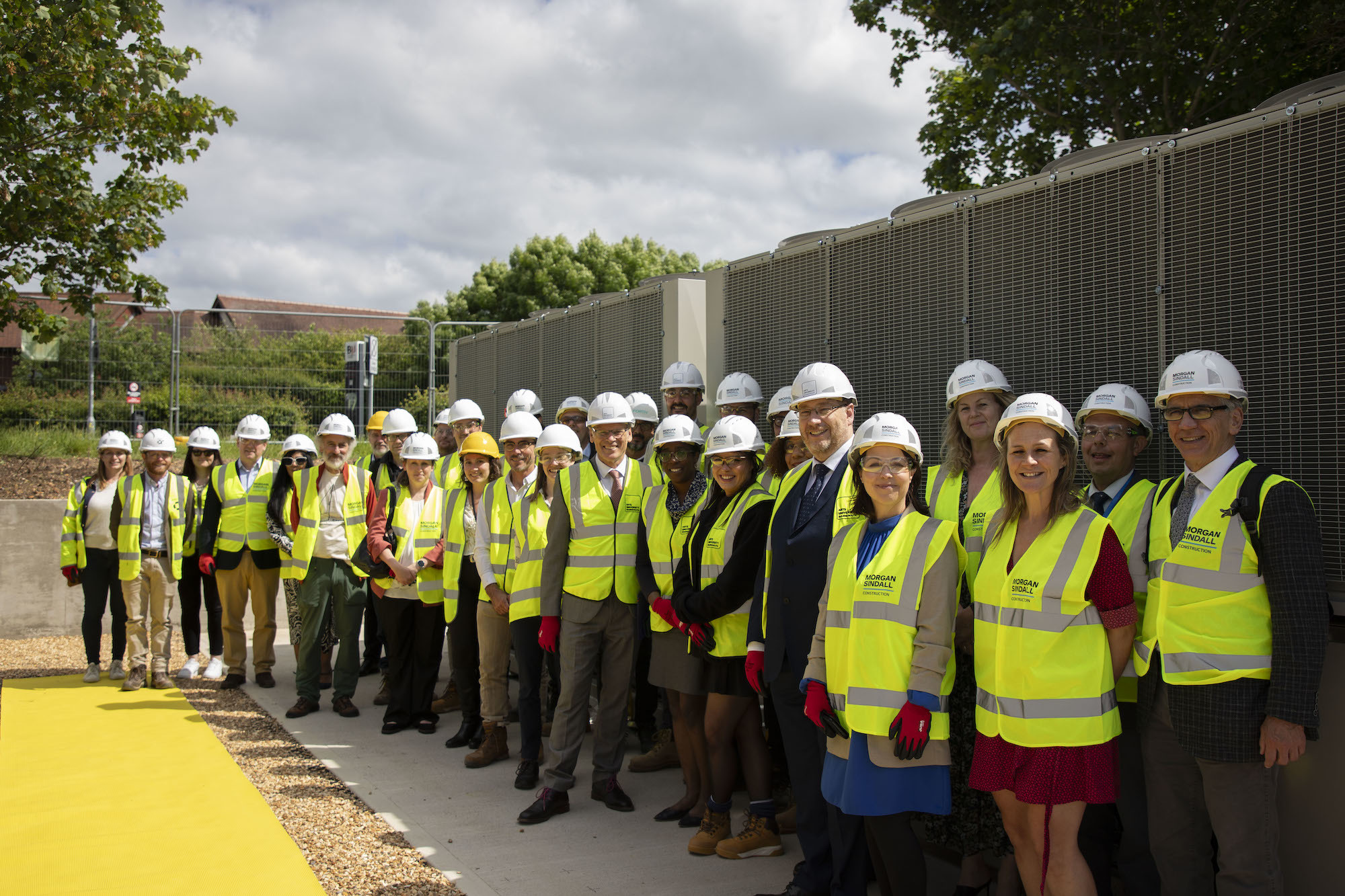 A large group of AUB staff gather next to newly installed air source heat pumps on AUB campus.