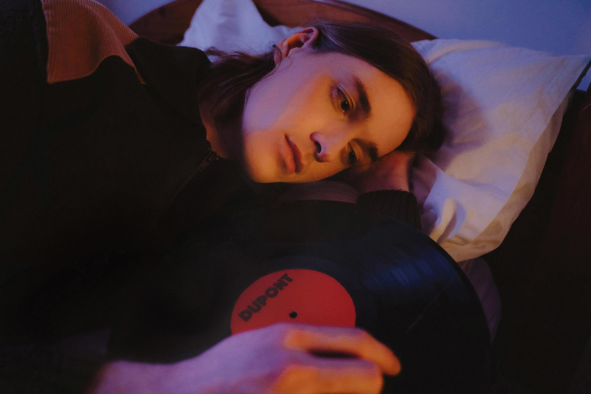 Boy in bed with a vinyl record, warm orange lighting.