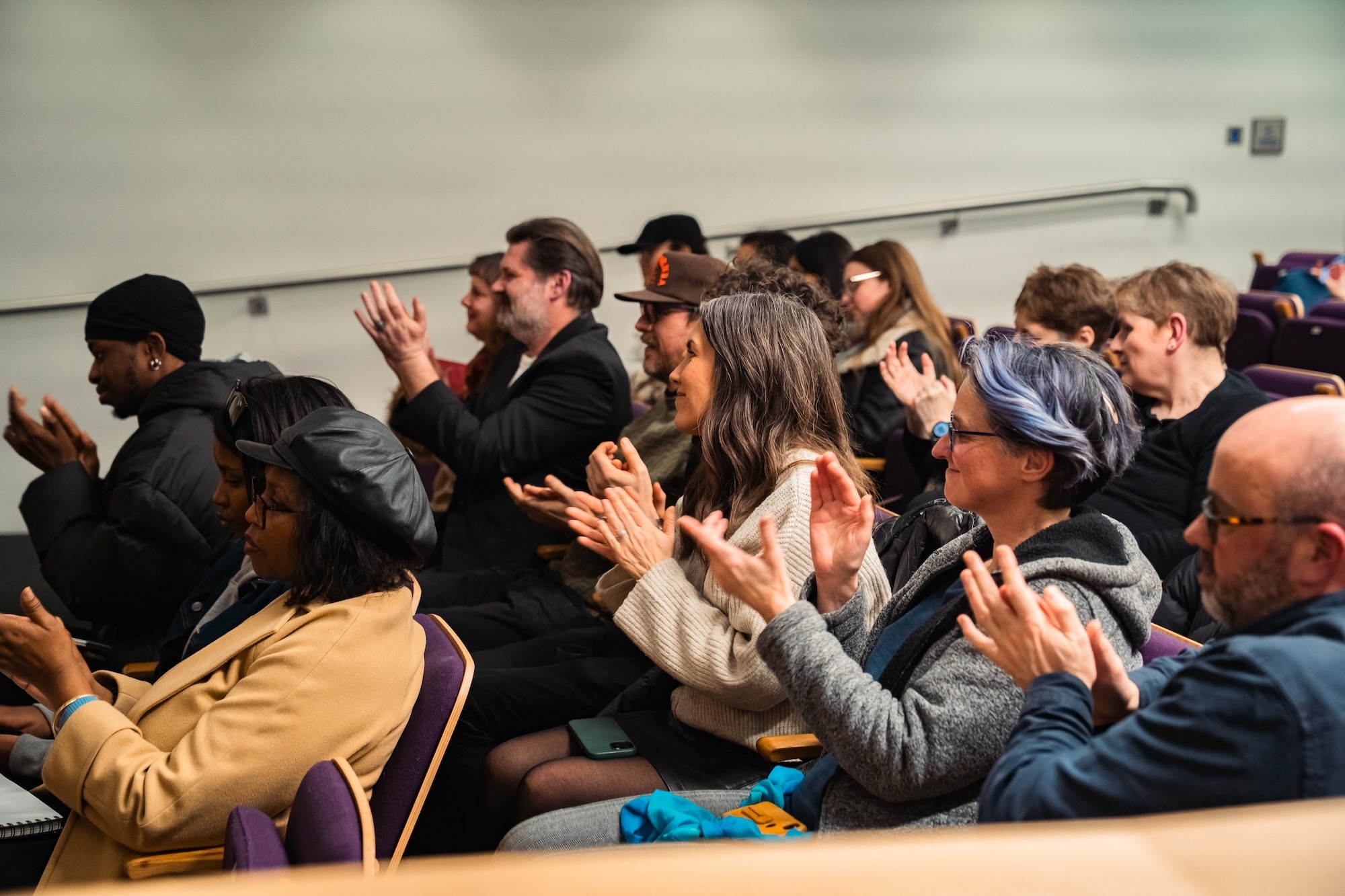 Several members of Arts University Bournemouth staff and visitors applauding from the audience in a lecture theatre.