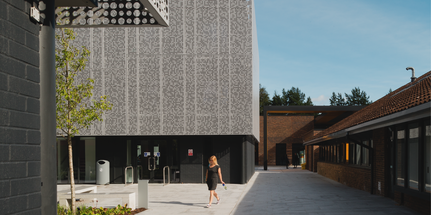 University building with a metal mesh exterior and a person walking in a courtyard outside.