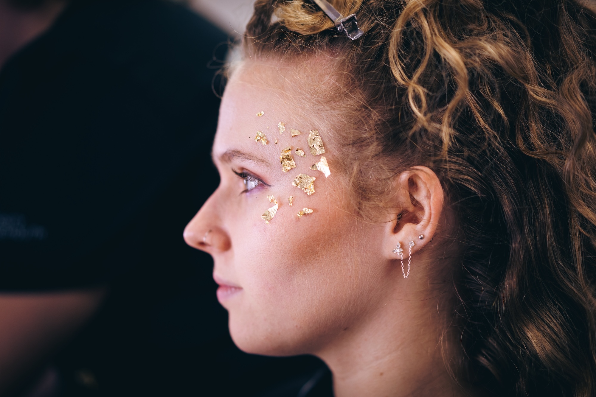Close-up of an Arts University Bournemouth student performer's face, viewed from the side, with flecks of gold leaf applied around their eye.