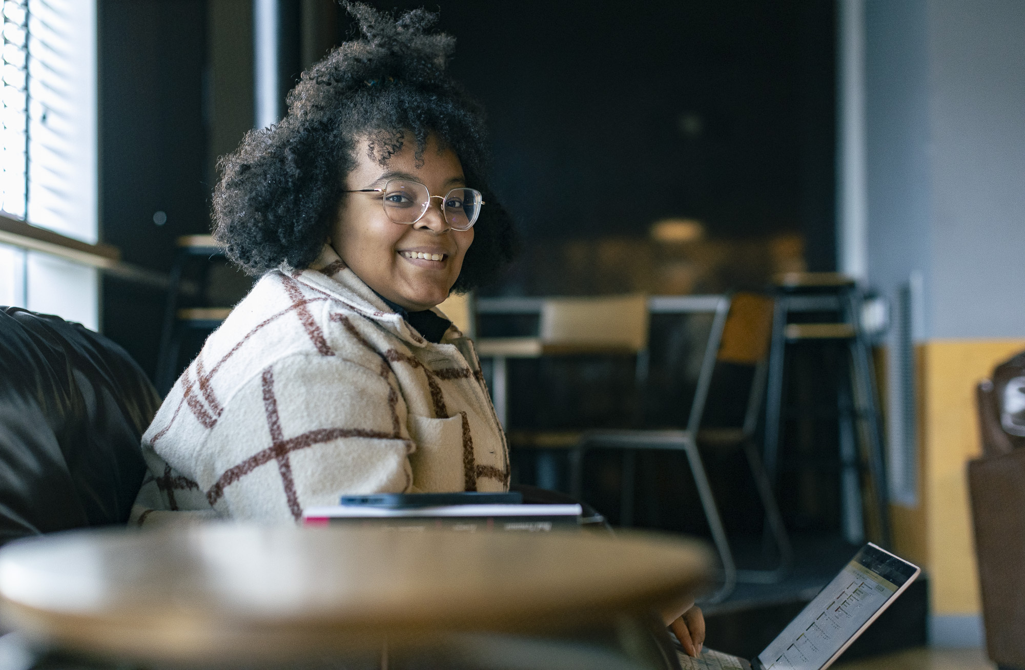 An Arts University Bournemouth student sits and works on a laptop, turning and smiling at the camera.