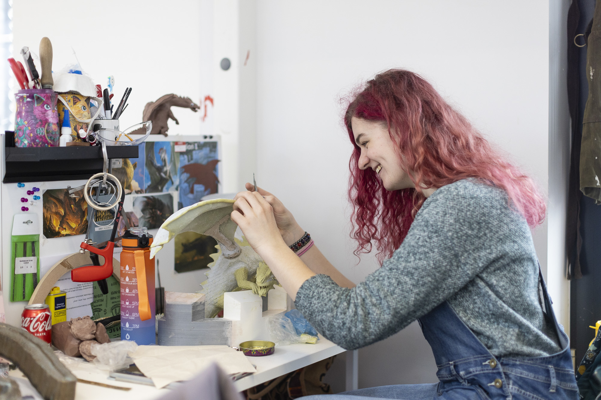 A BA (Hons) Modelmaking student sitting at a work station constructing a model of a dragon.