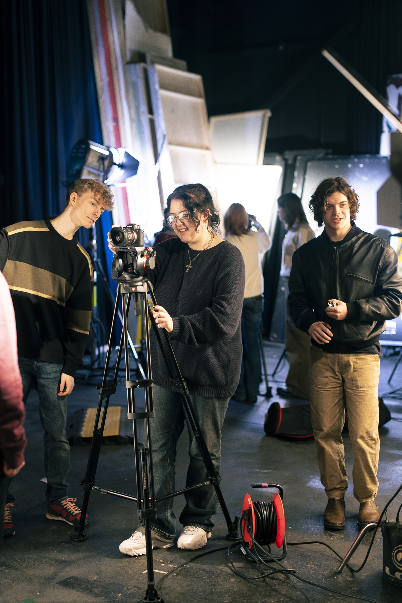 Three Arts University Bournemouth students on film set with camera on tripod, lighting equipment, and geometric white backdrop structures