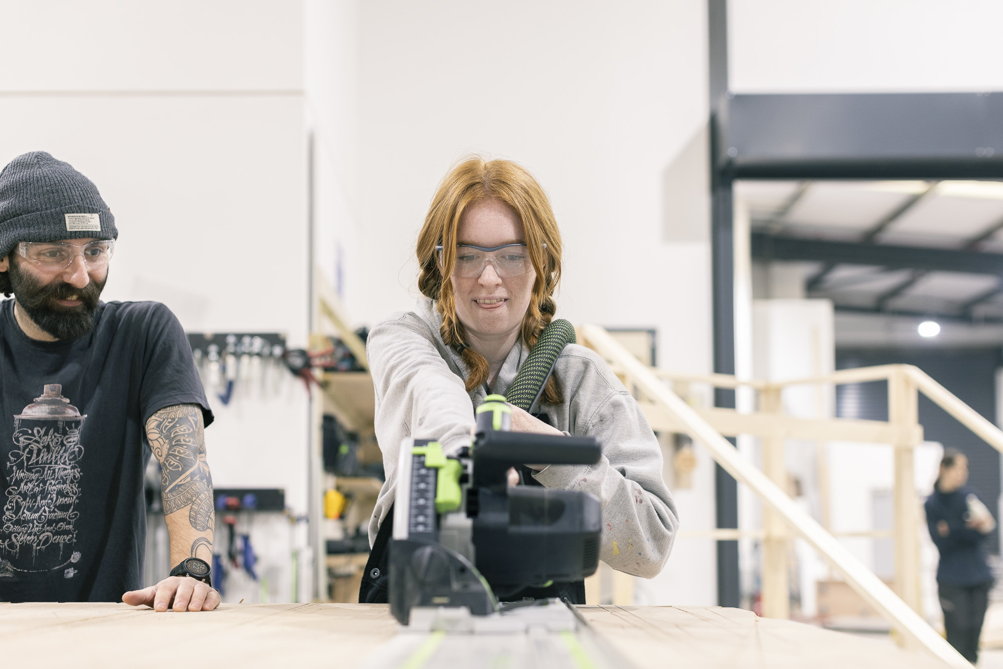 An AUB student using a power saw on a piece of wood in the on-campus workshop, supervised by a technician.