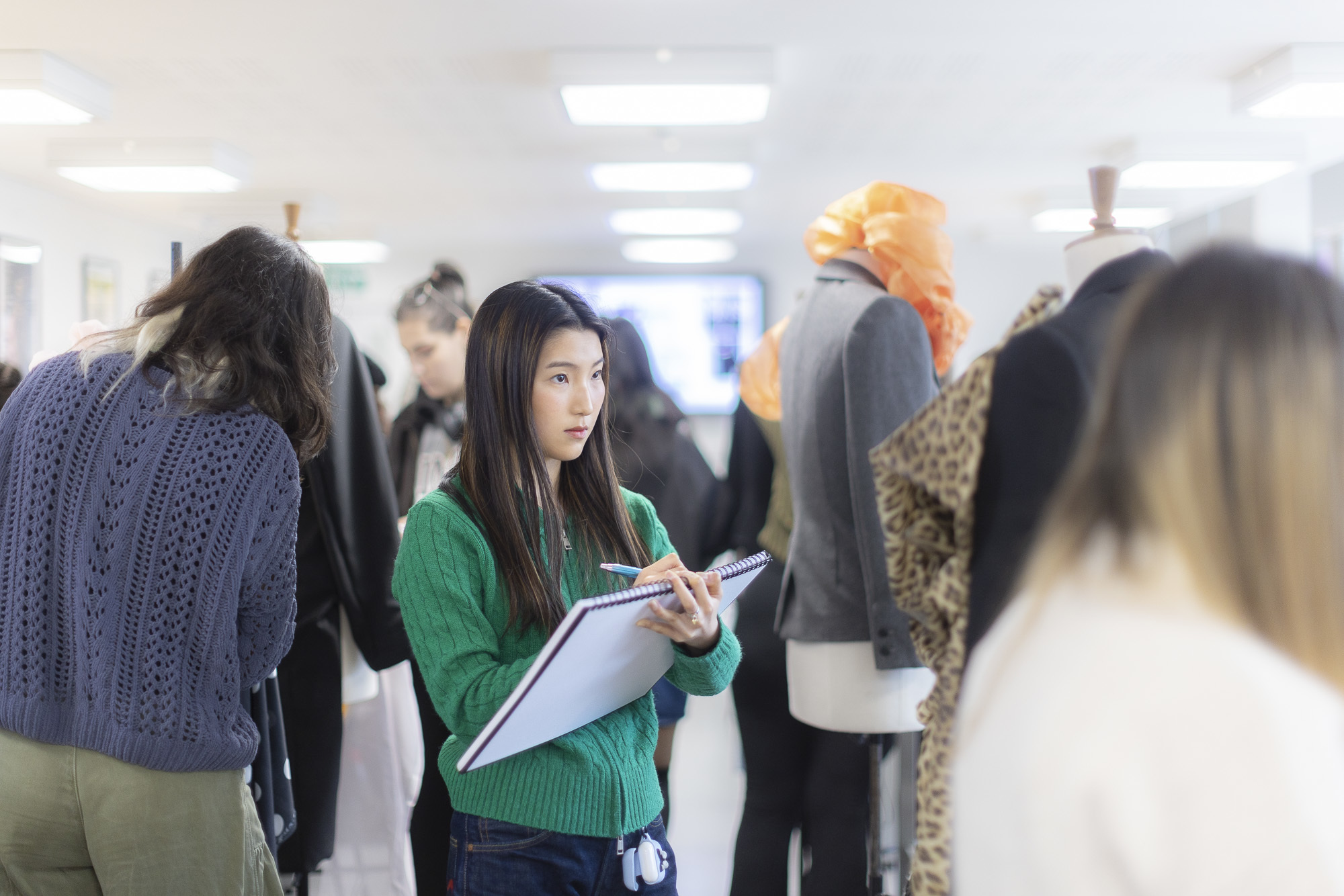 A student drawing in a sketchbook and focusing on a costume on a mannequin.