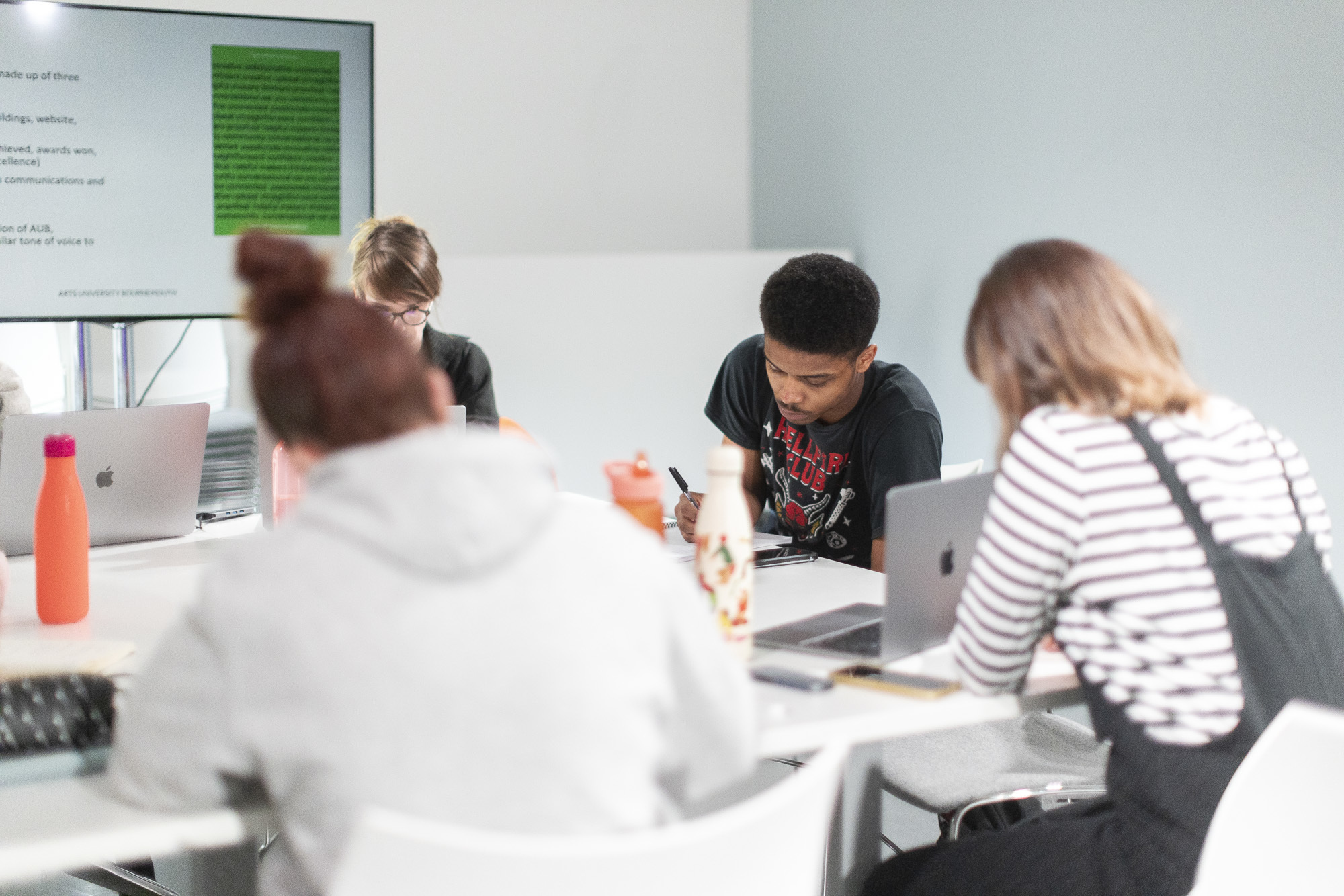 Four AUB students sitting at desks in a seminar room, working on laptops and notebooks.