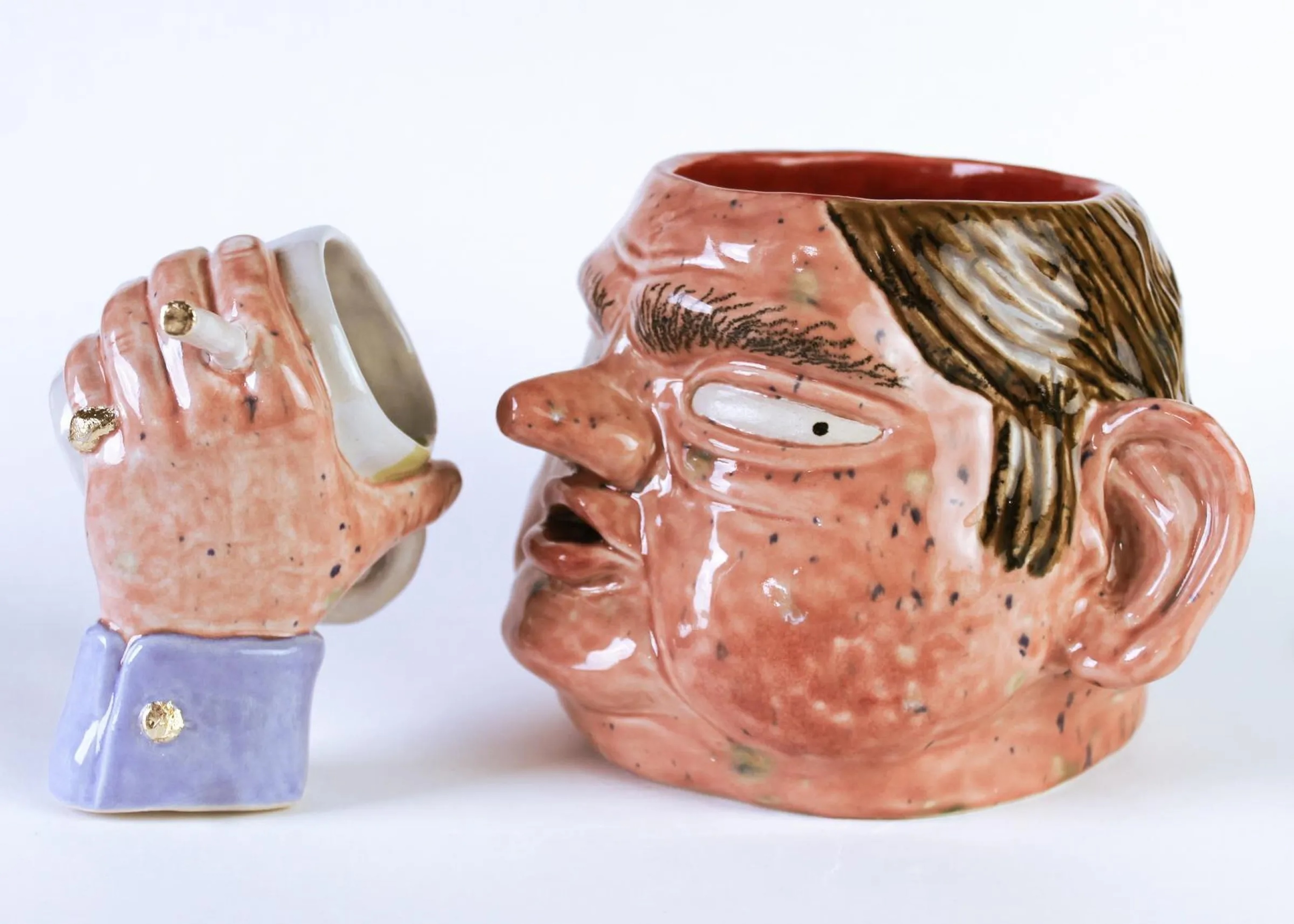 Ceramic mug shaped like man's head with brown hair and pink face, next to matching hand-shaped mug with blue cuff and gold details.