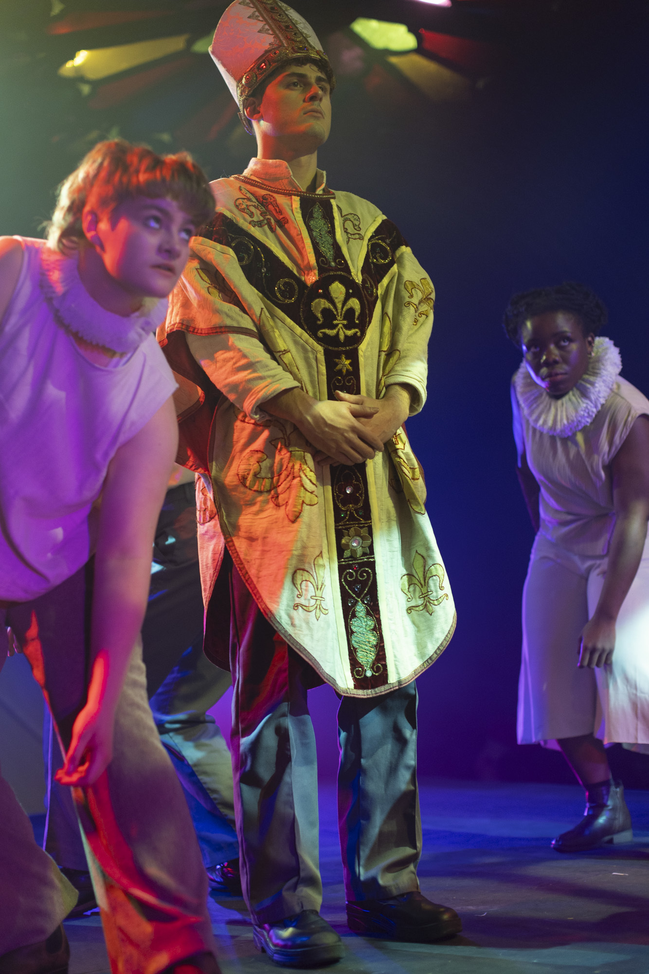 Three BA (Hons) Acting students in costume while performing "I, Joan". The actor in the centre is wearing a cassock and mitre as a pope; the others are leaning forward, wearing ruffs around their necks.