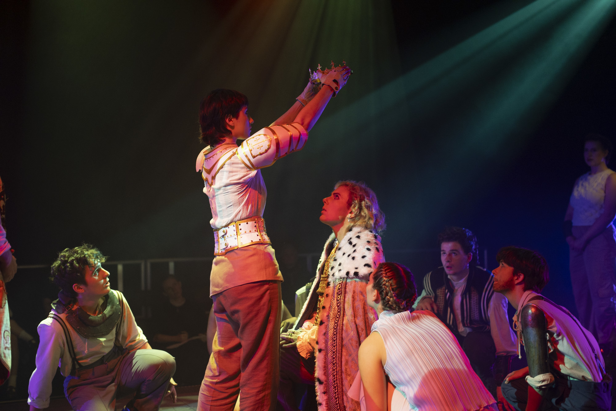 BA (Hons) Acting students performing I, Joan. Most actors are kneeling, including one dressed as a king. An actor playing Joan of Arc is standing, viewed from the back and holding a crown above the king's head.