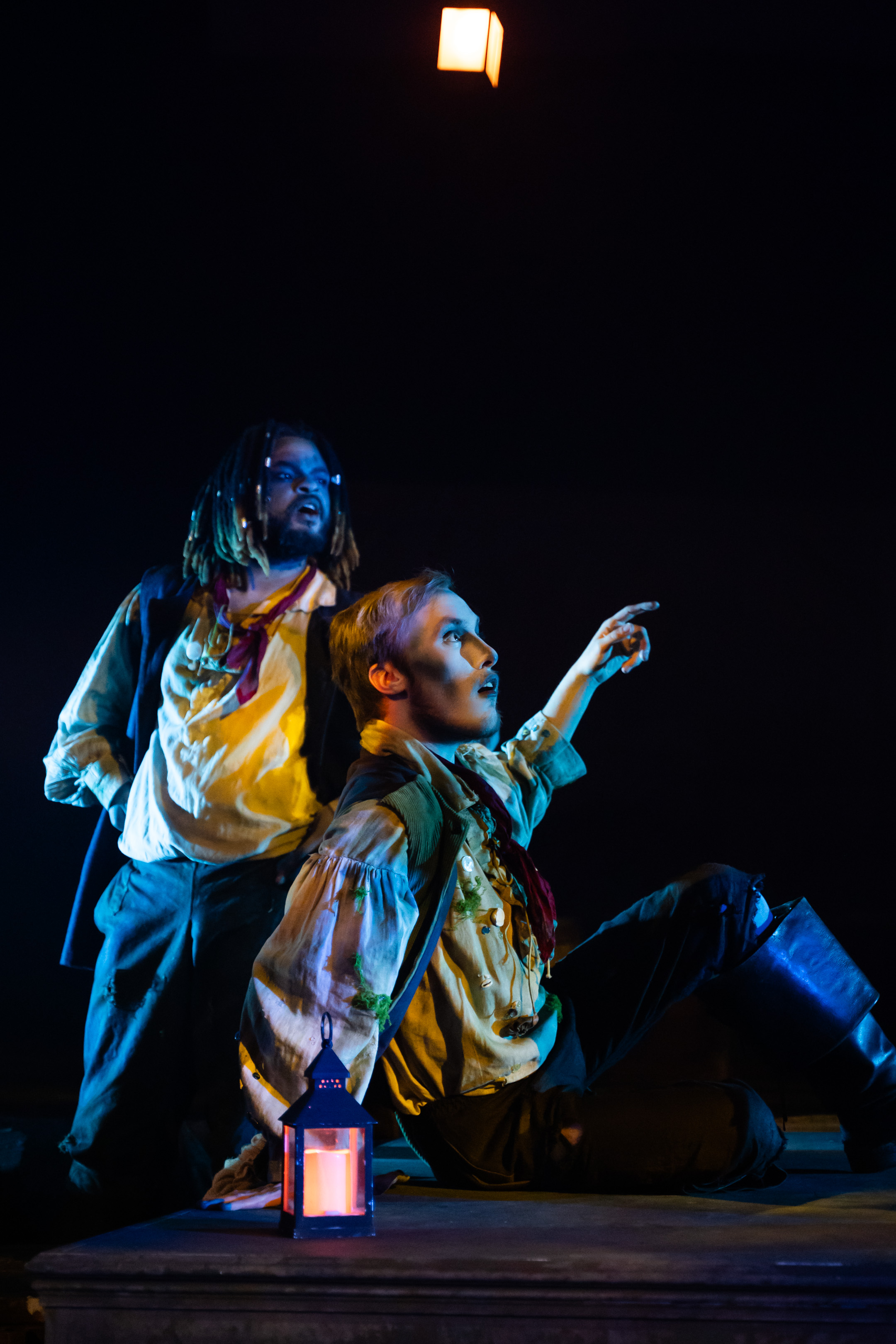 Two BA (Hons) Acting students in period costume performing in "Moonfleet". One is sitting on the ground, the other standing, both looking off to the right in surprise.