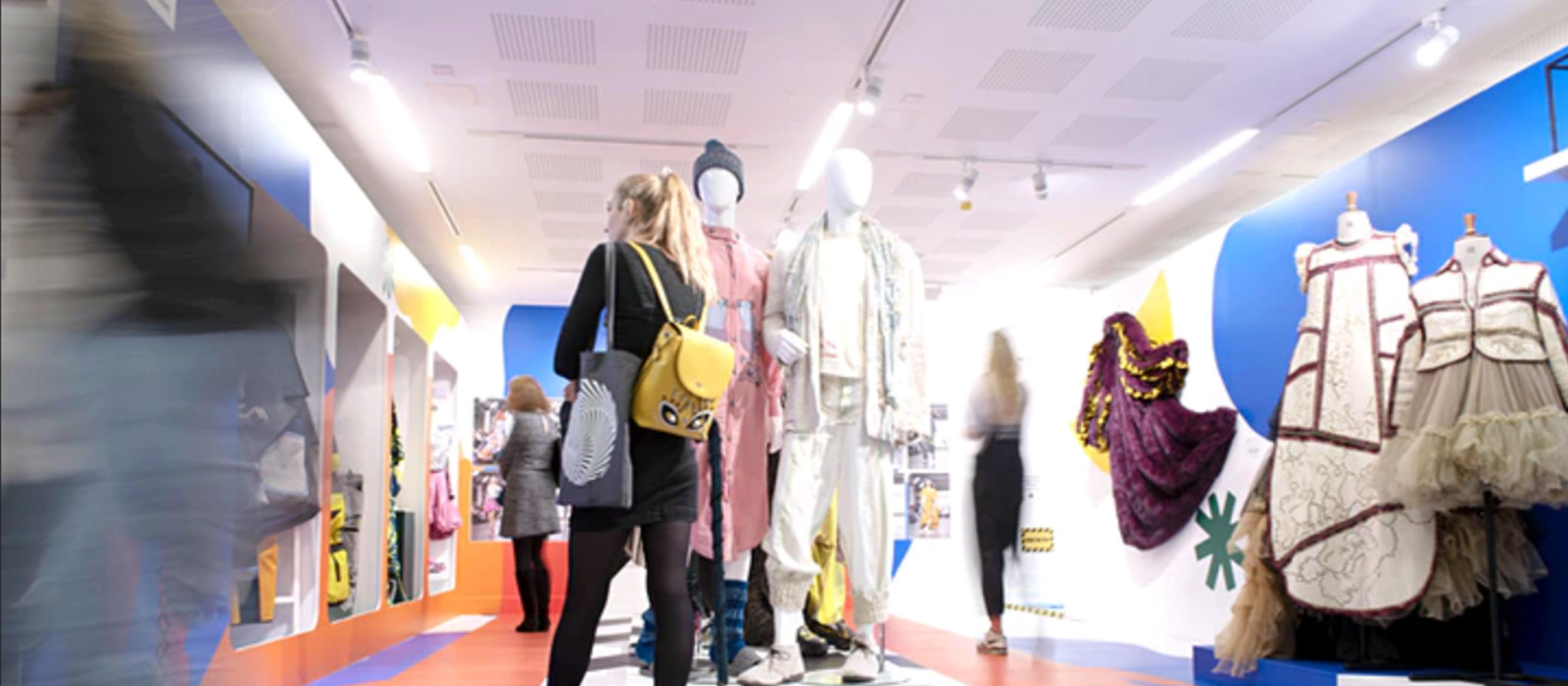 Person walking through a gallery space. There are costumes on mannequins and attached to the walls.