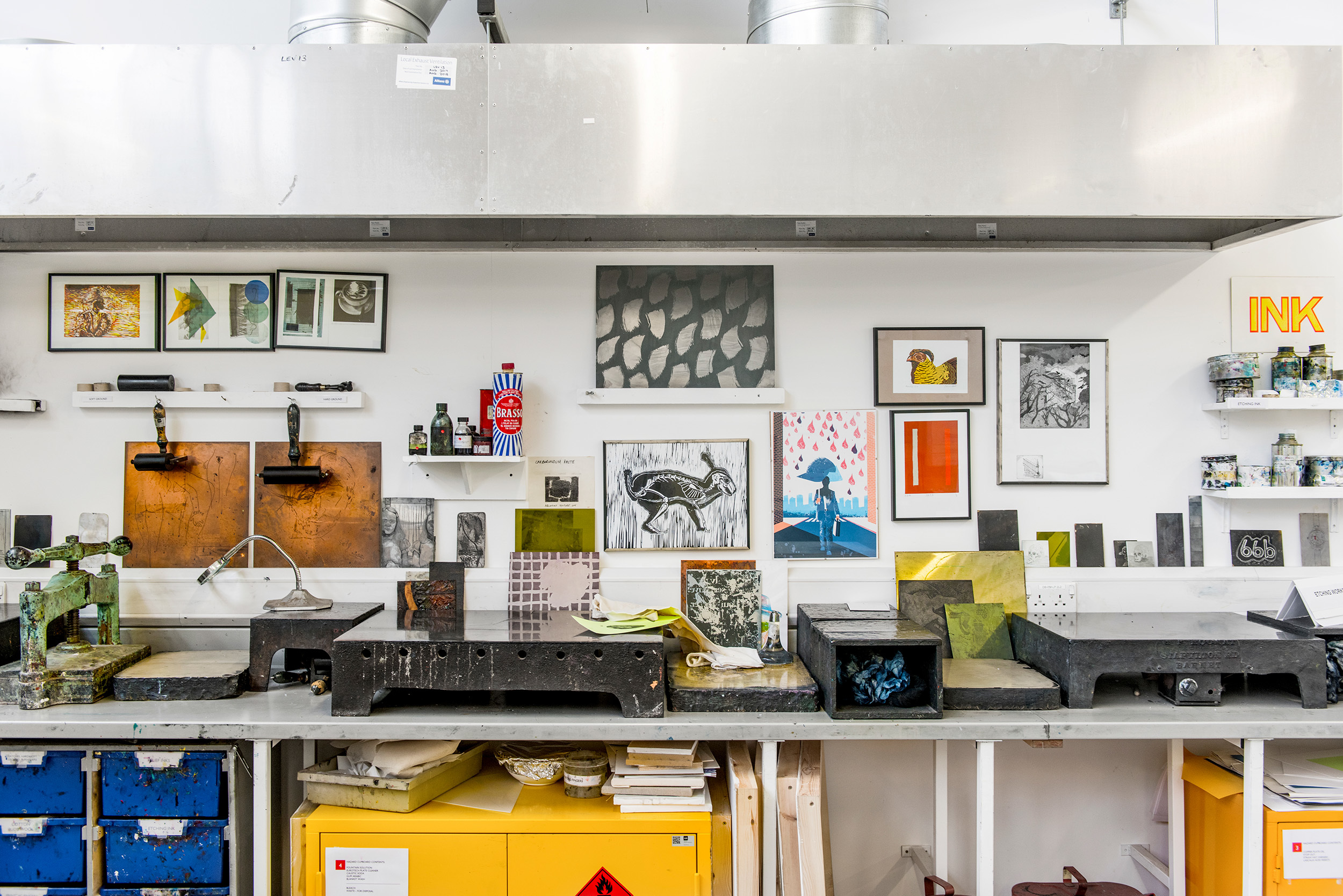 A wall in the print room at AUB, the wall is lined with printmaking equipment including rollers, oils and artwork and a bench for inking up