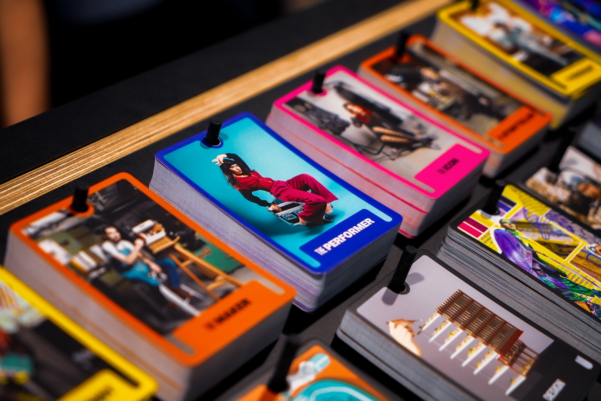 Selection of colourful cards on a black pegboard with pink, blue, orange and yellow borders, focused in on 'The Performer'.