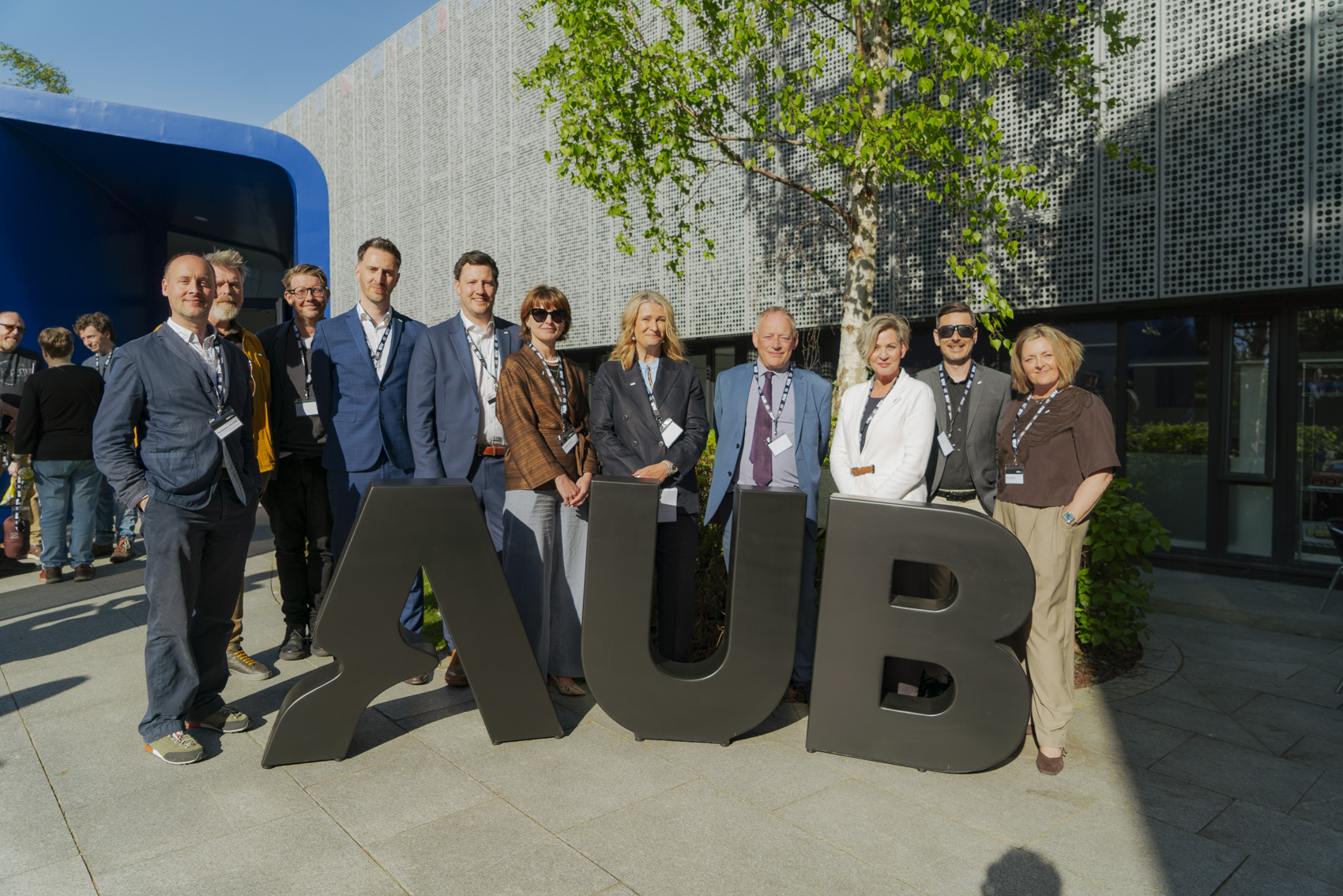 Several members of the Arts University Bournemouth senior leadership team pose for a photo behind giant AUB letters.