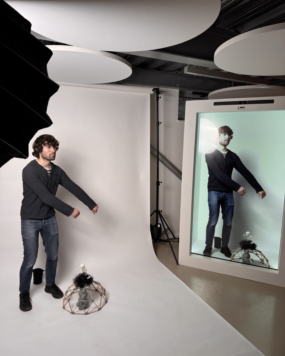 Staff member posing with object on ground in front of white background, to the right is a hologram projection of him in the Holobox.