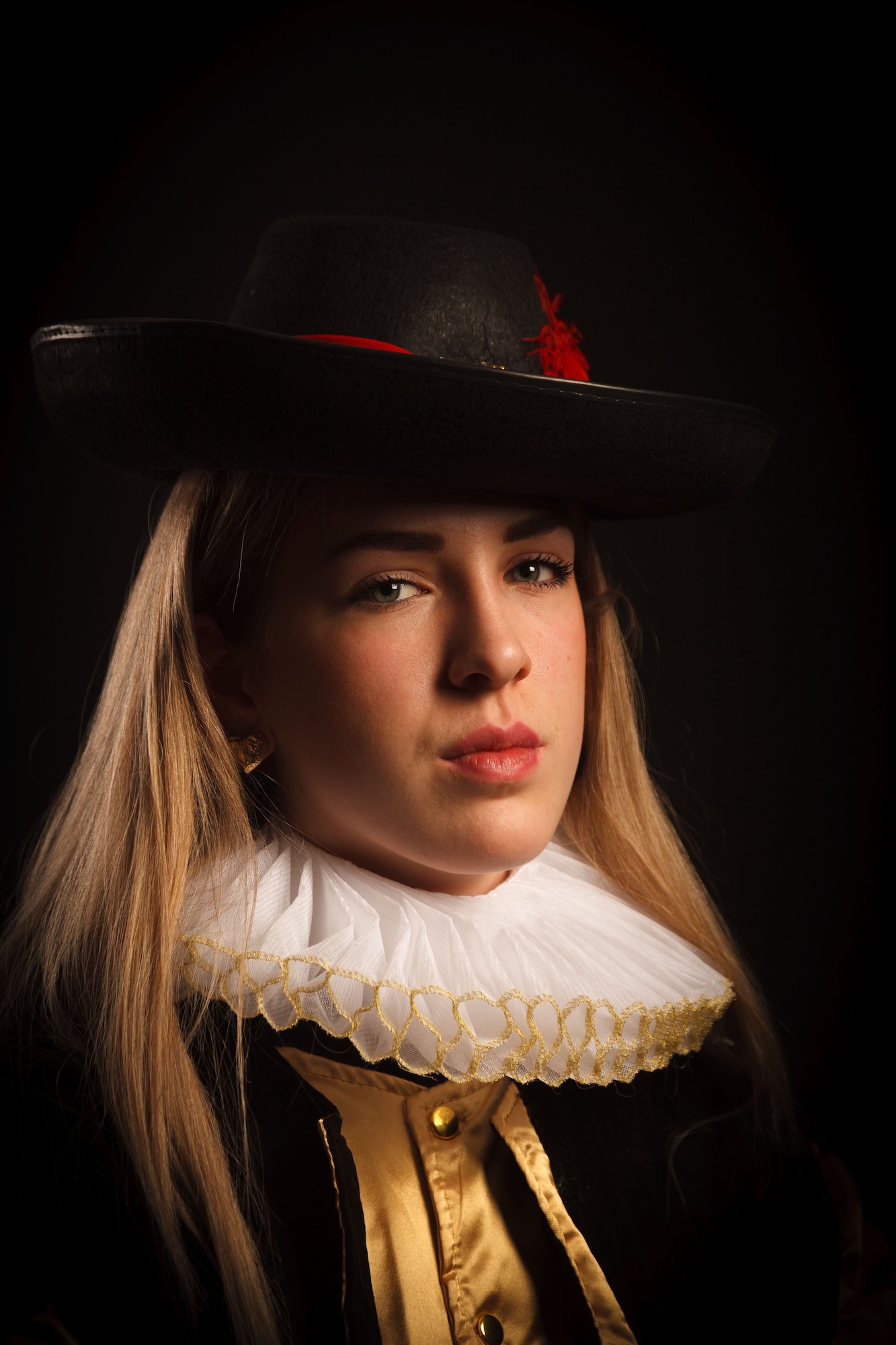 A young woman with long blonde hair wears a black hat and an elaborate collar. The collar is white with a ruffled design, while her outfit features rich colours. The background is dark, highlighting her features and the details of her attire.