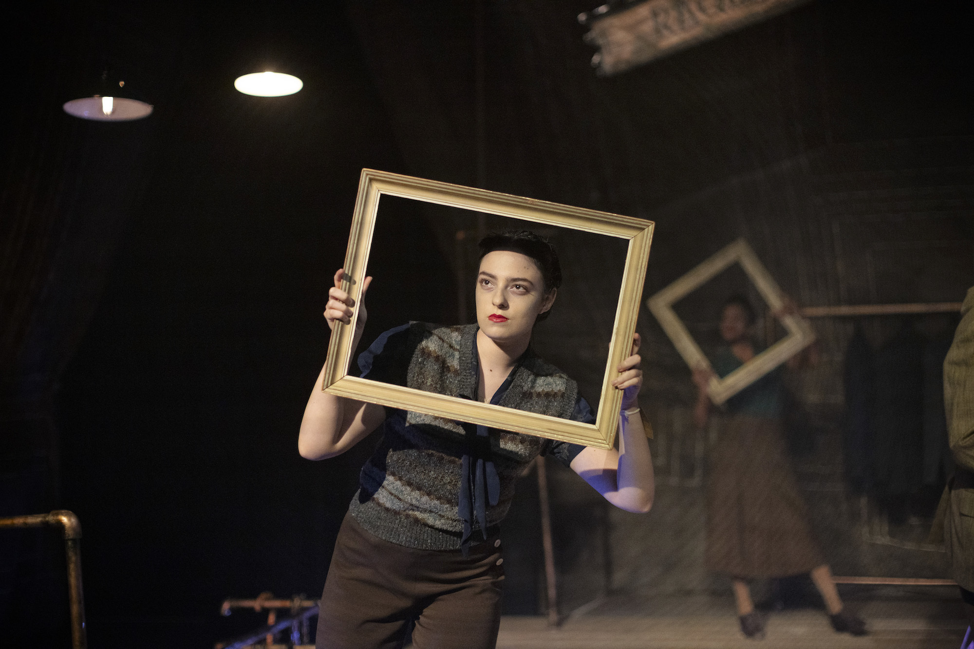 A BA (Hons) Acting student dressed in 1940s style costume holds an empty picture frame up to their face.