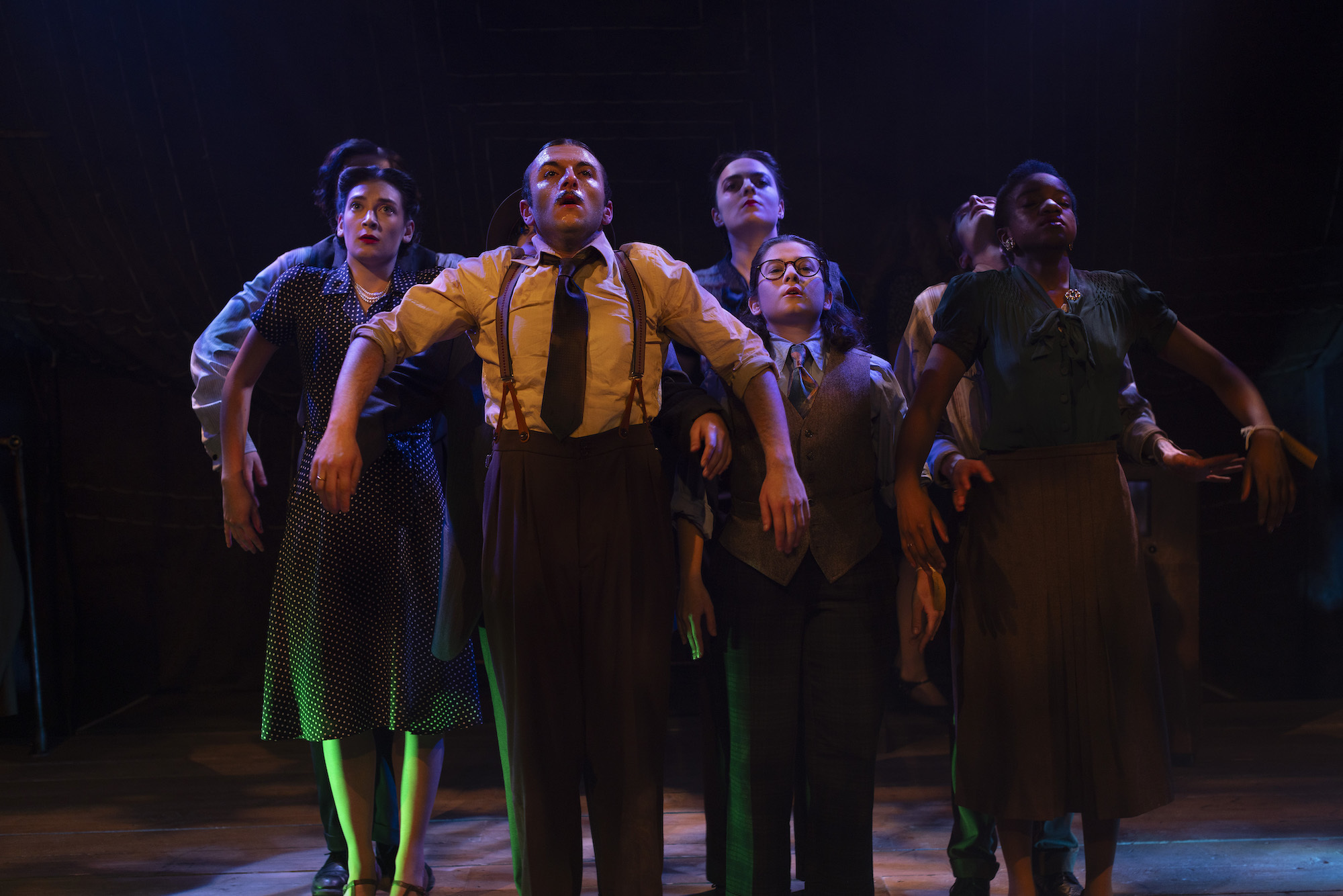 A group of BA (Hons) Acting students in 1940s style costume on stage while performing "Thérèse". All are stood with their shoulders raised.