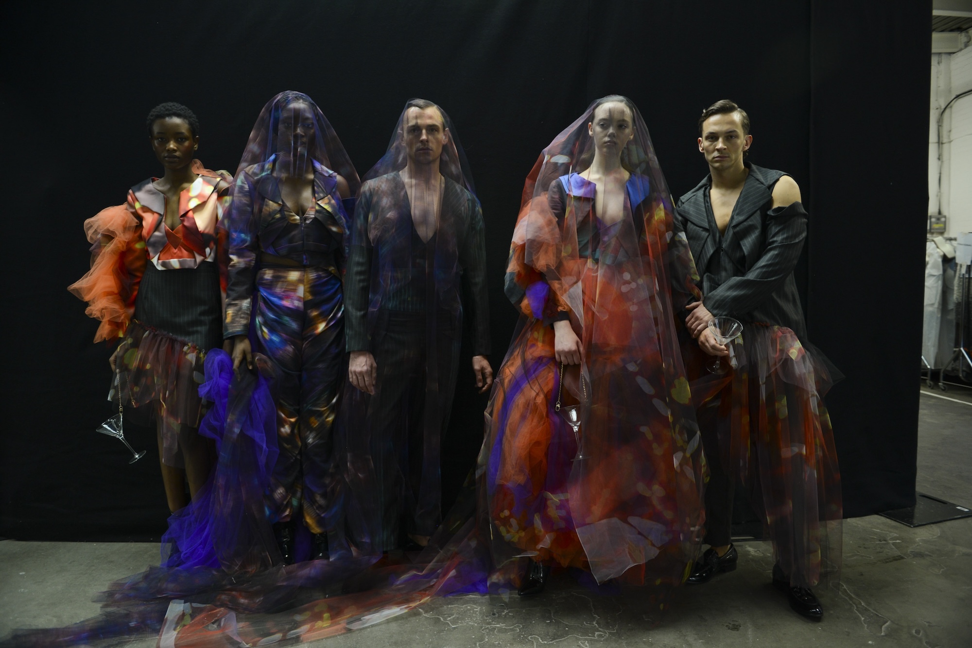 Five models in various colourful and abstract garments from the collection 'Happy Hour' by J Mitchener, posing for a photo backstage at Graduate Fashion Week